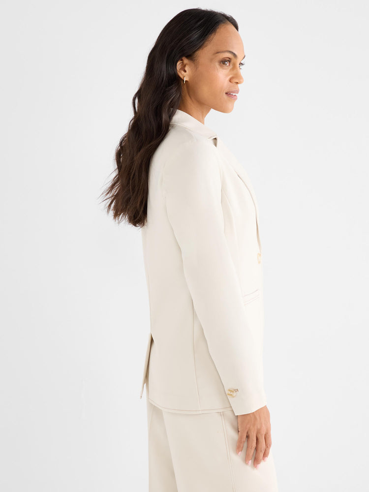 Model wears a tailored cream blazer and matching wide-leg trousers in a smooth, classic fit shown in a side profile view.