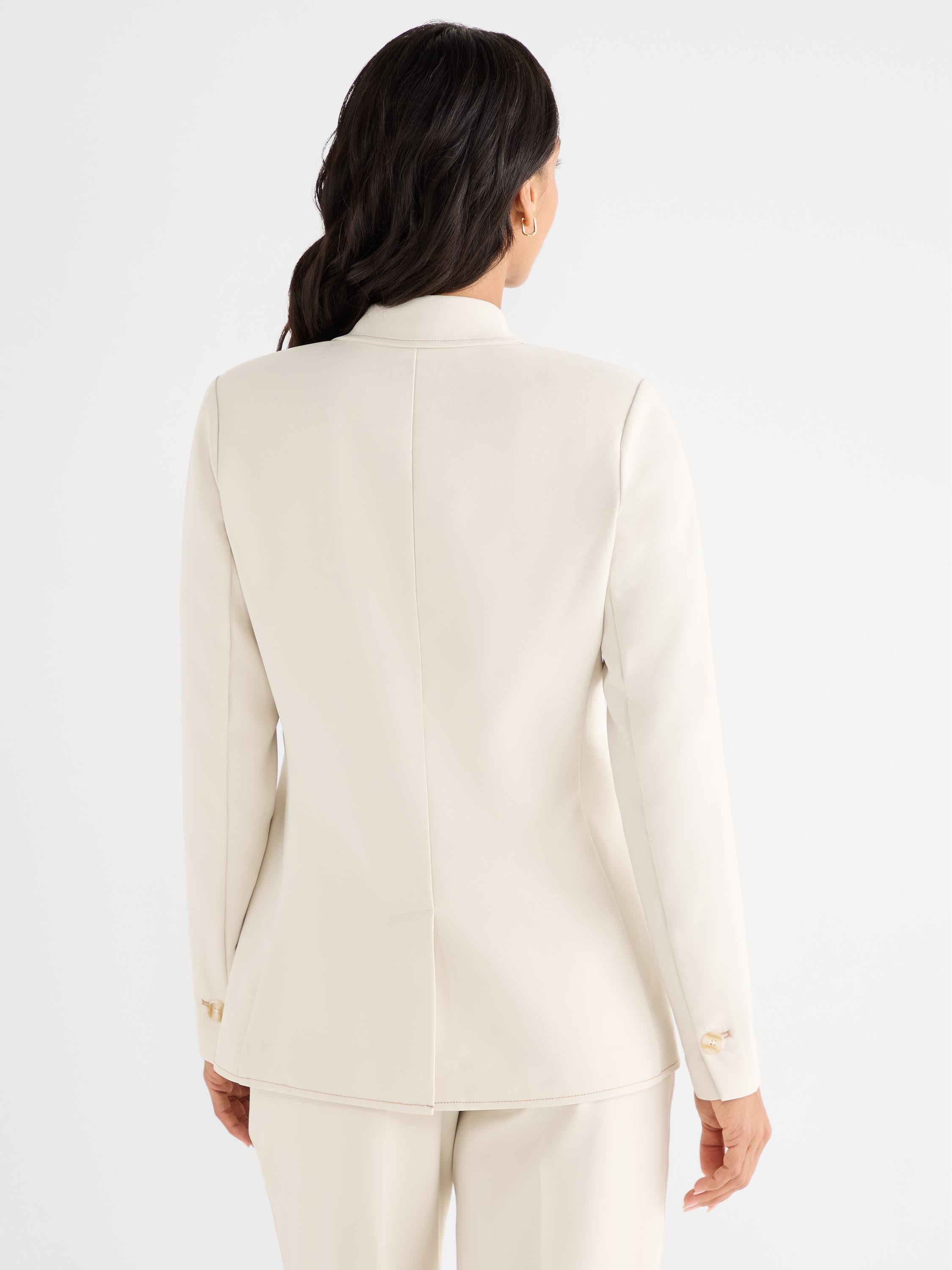 The model wears a fitted cream blazer from the back, featuring a standing collar and cuff button detail.