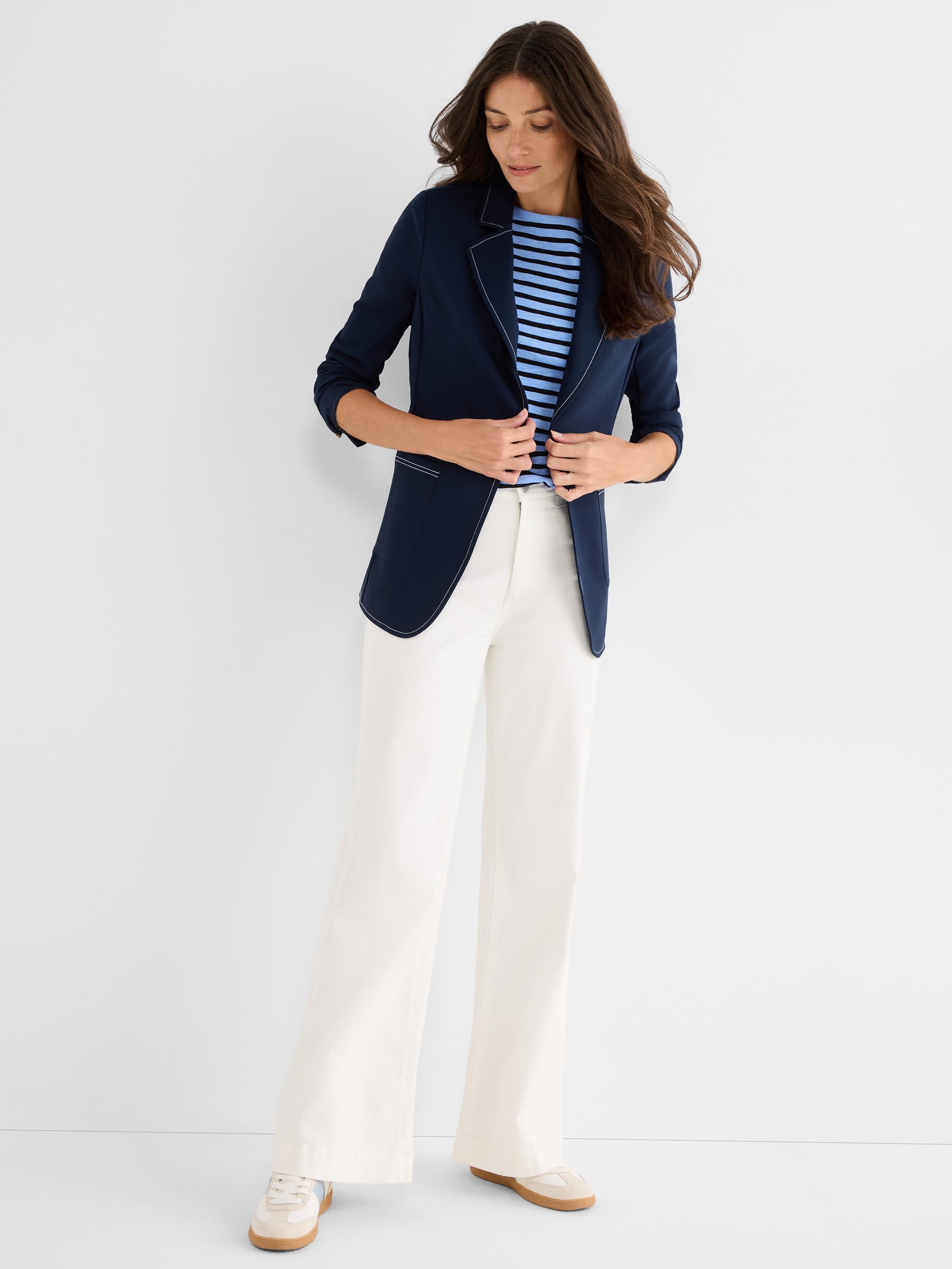A tailored navy blazer with white contrast stitching is paired with relaxed, high-waist cream wide-leg trousers and a.