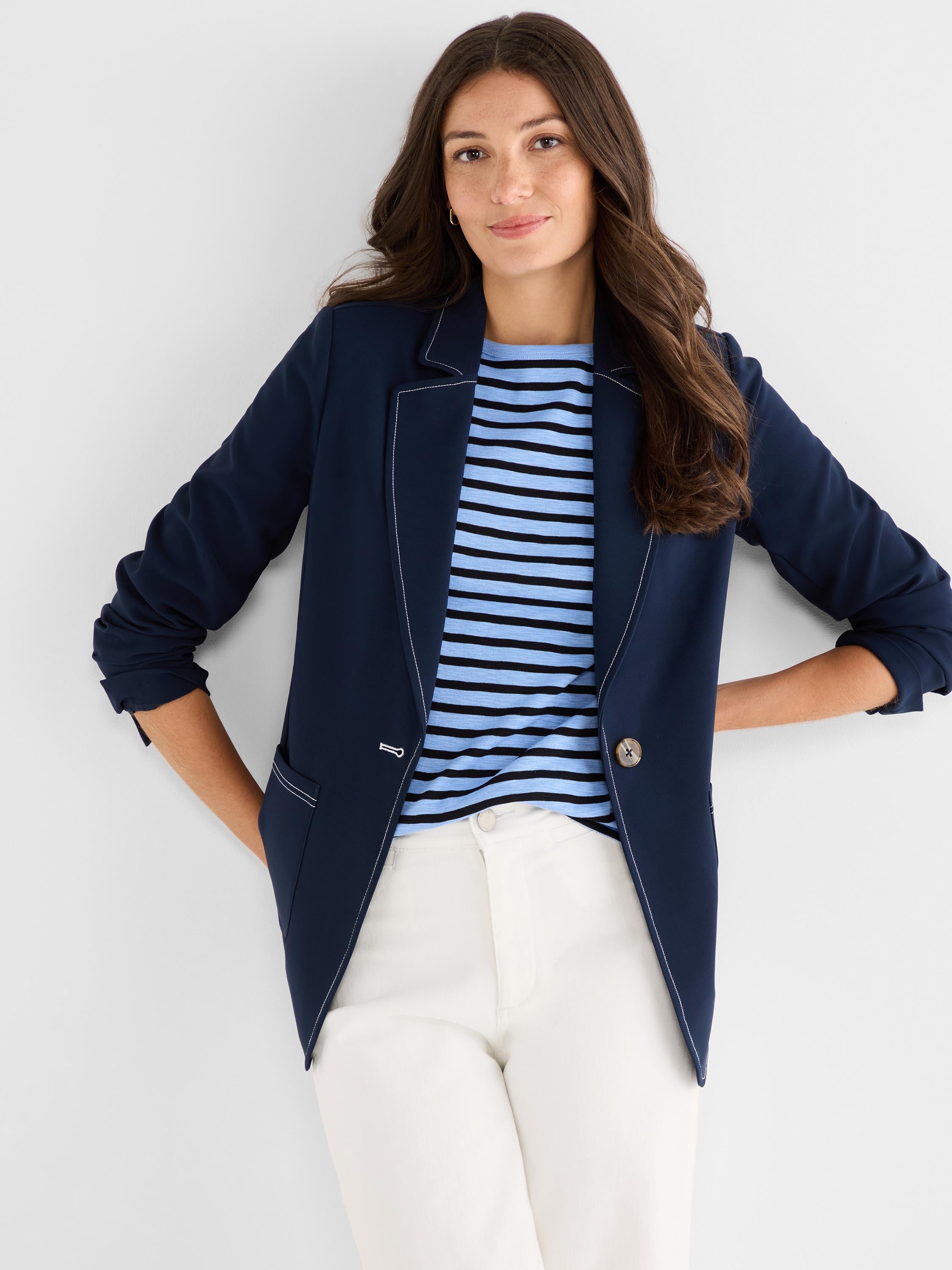 A tailored navy blazer featuring bold white contrast stitching along the lapels, seams, and pockets is worn open.