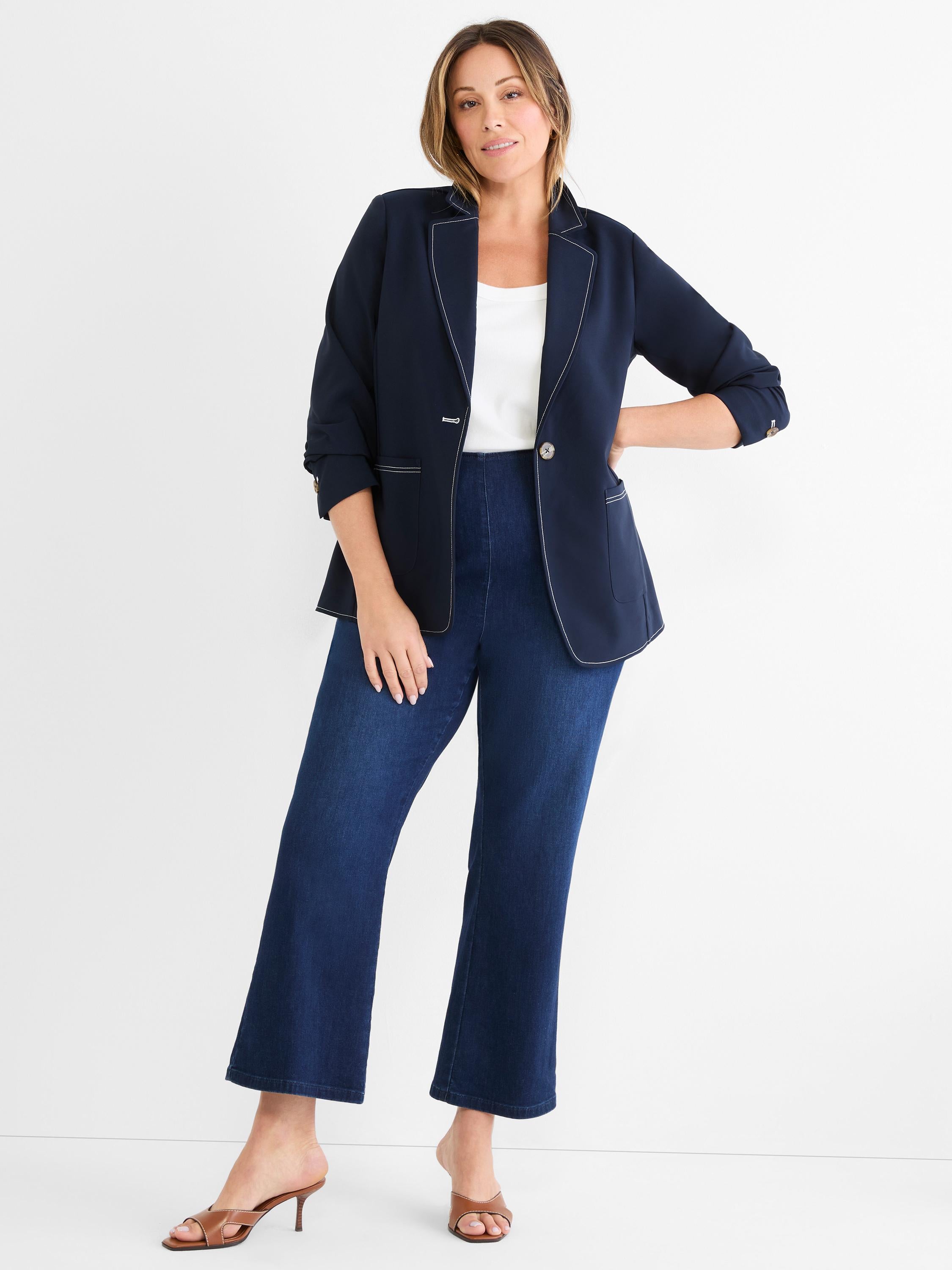 Model wears a navy single-breasted blazer with crisp white contrasting topstitching and three-quarter length cuffed sleeves.
