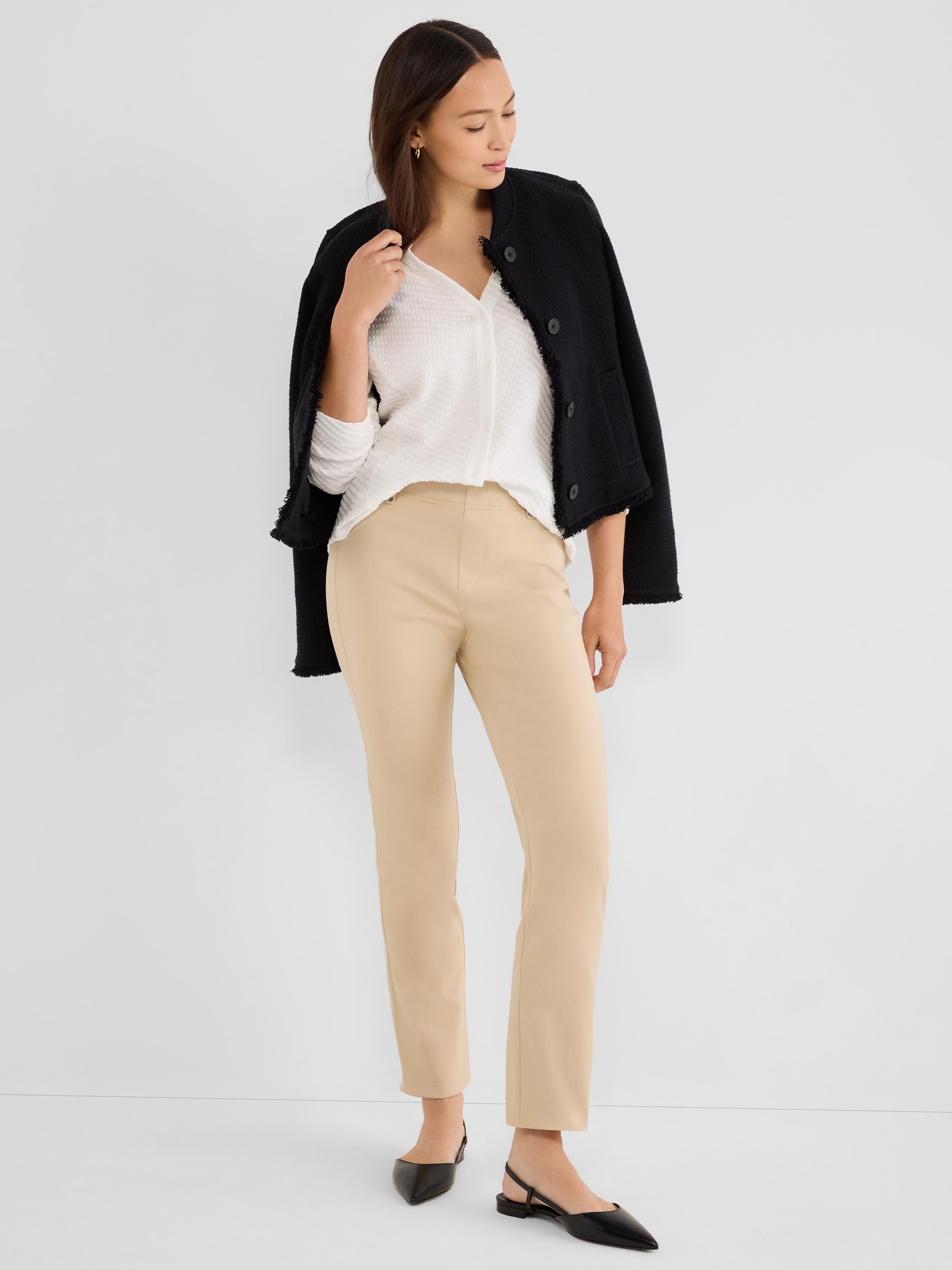 The model wears slim beige ankle-length trousers styled with a white blouse and black textured jacket.