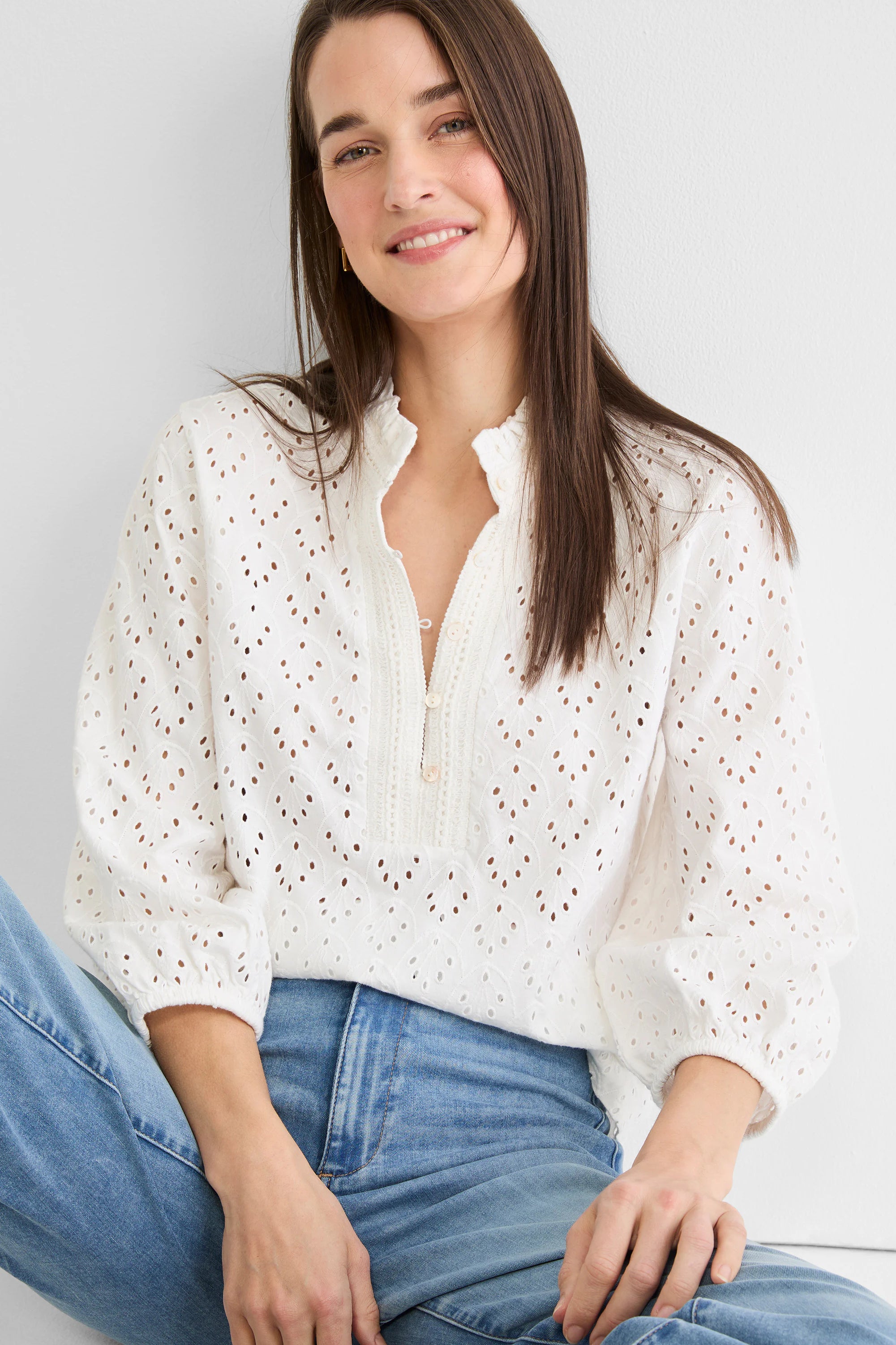 White knit eyelet top with ruffle neck, partial button placket, and gathered long sleeves.
