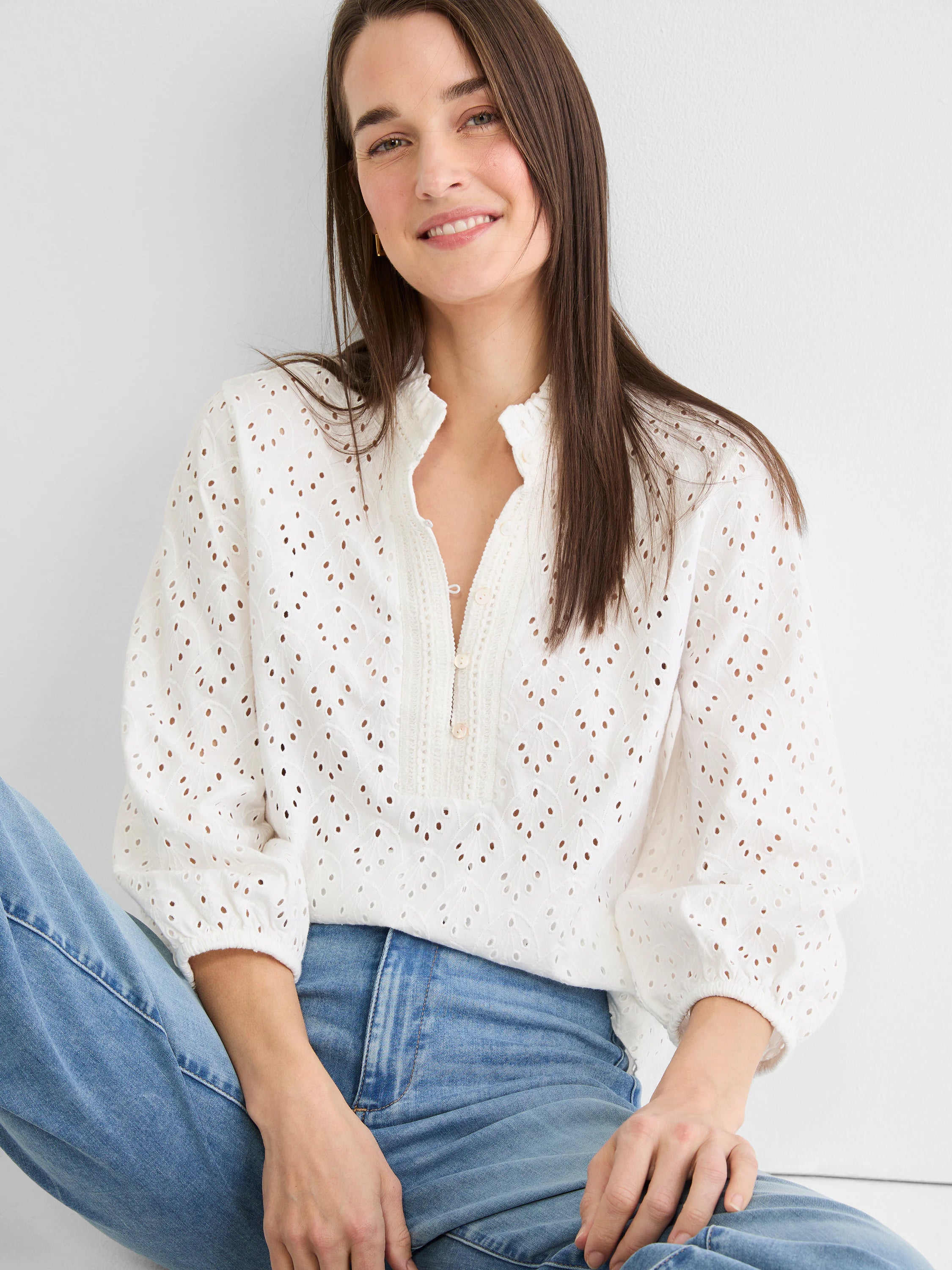 White knit eyelet top with ruffle neck, partial button placket, and gathered long sleeves.