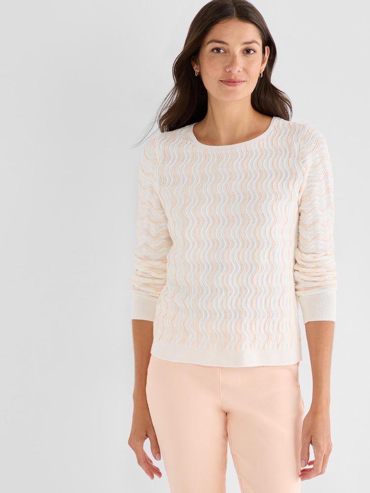 Model wears a white crewneck sweater with peach wavy textures and long sleeves paired with slim peach trousers.