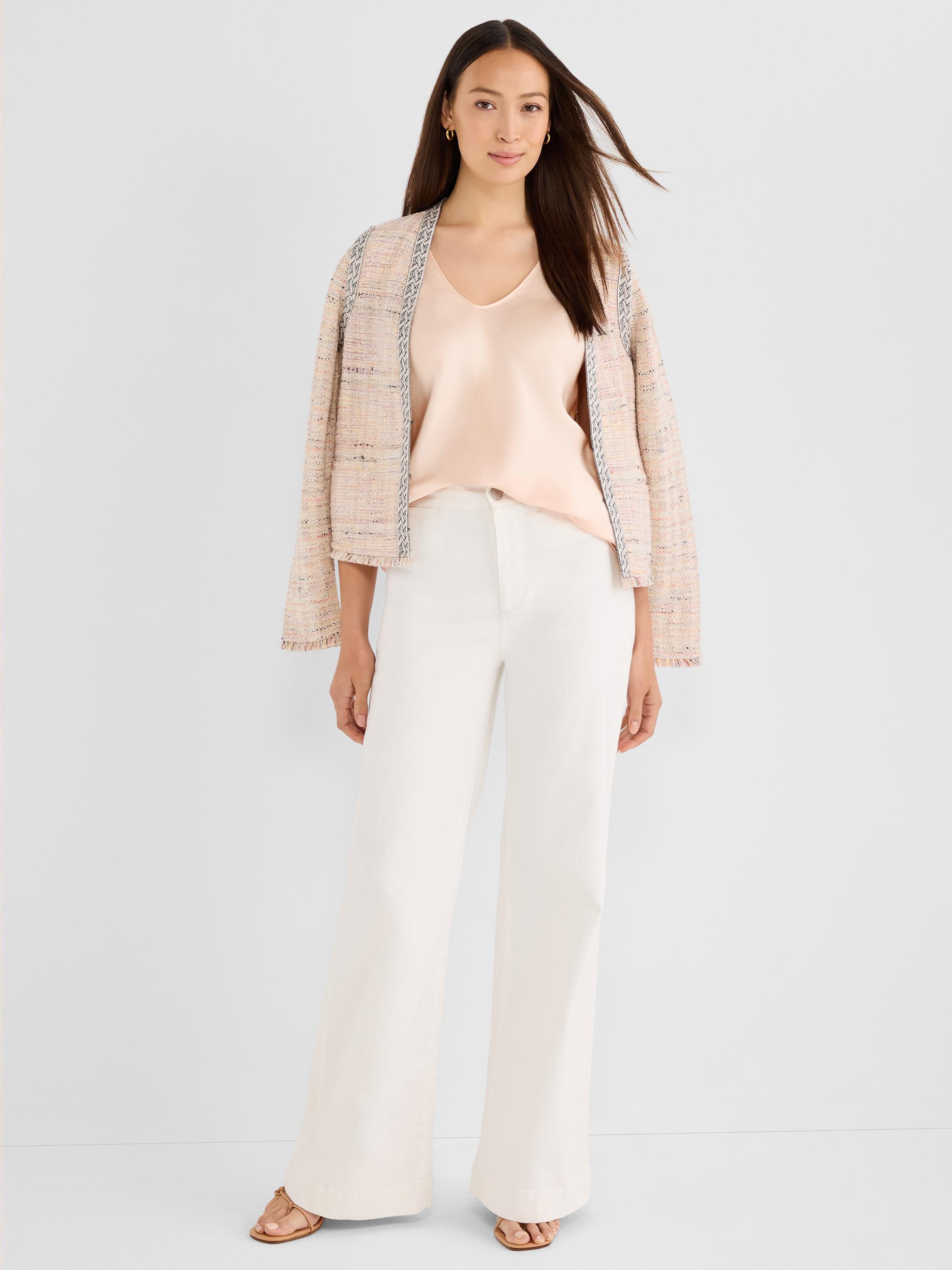 A model in a cropped pink tweed jacket featuring patterned trim and flowy ivory wide-leg trousers with a blush camisole.