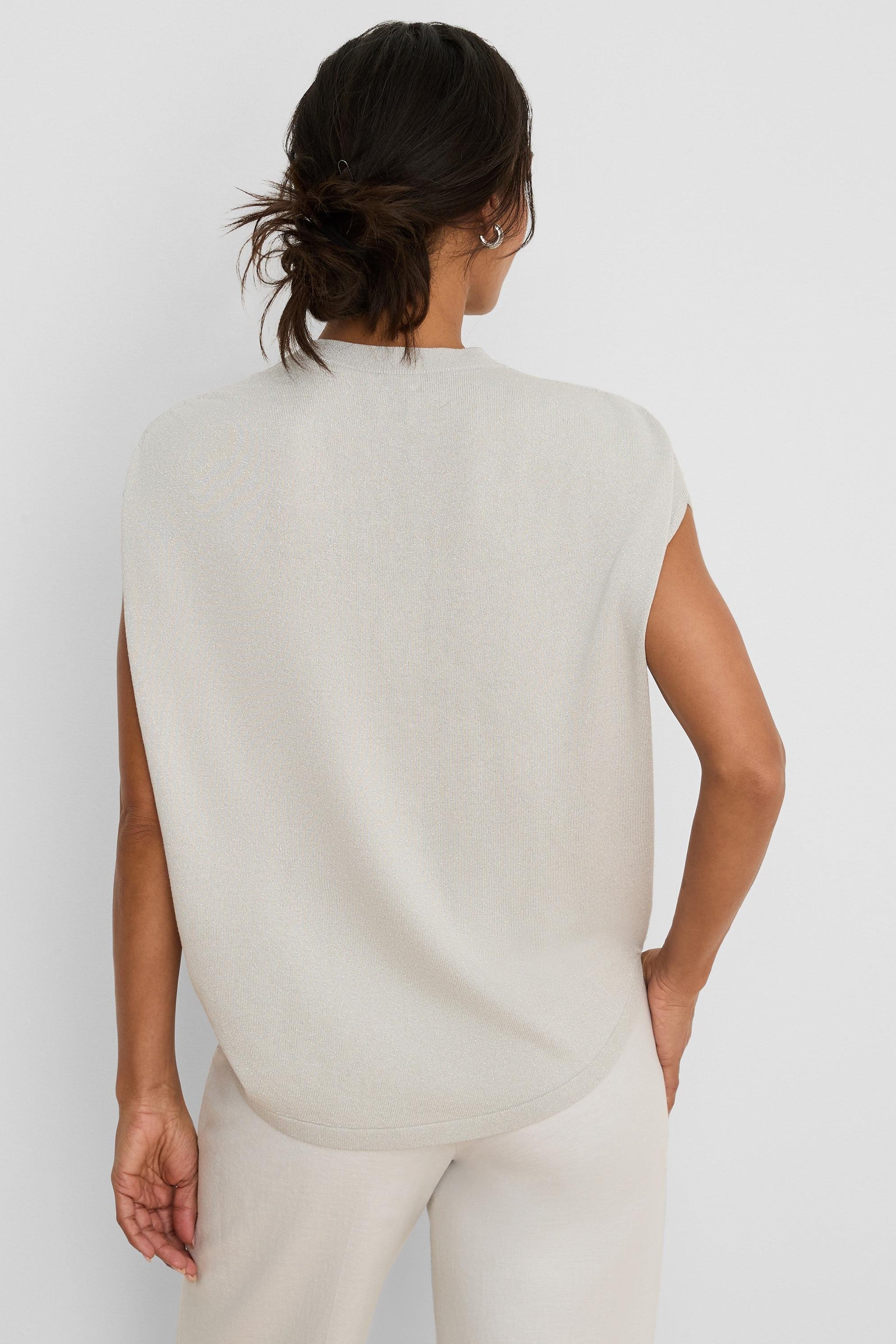 Back of a pale beige, sleeveless knit sweater with a mock neck. Features a relaxed fit and rounded hem.