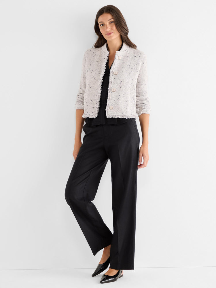 Cropped, collarless white knit jacket featuring a bouclé texture, dark flecks, button front, and frayed edges.