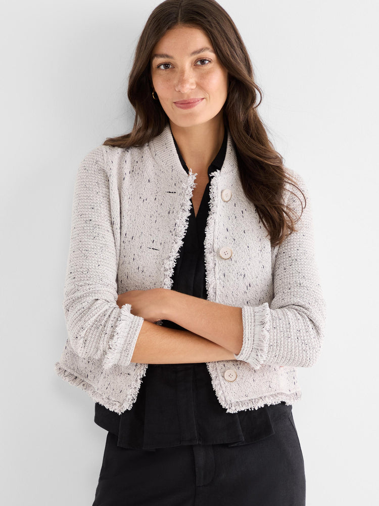 Model wears a collarless, cropped ivory tweed jacket featuring three buttons and raw fringe trim.