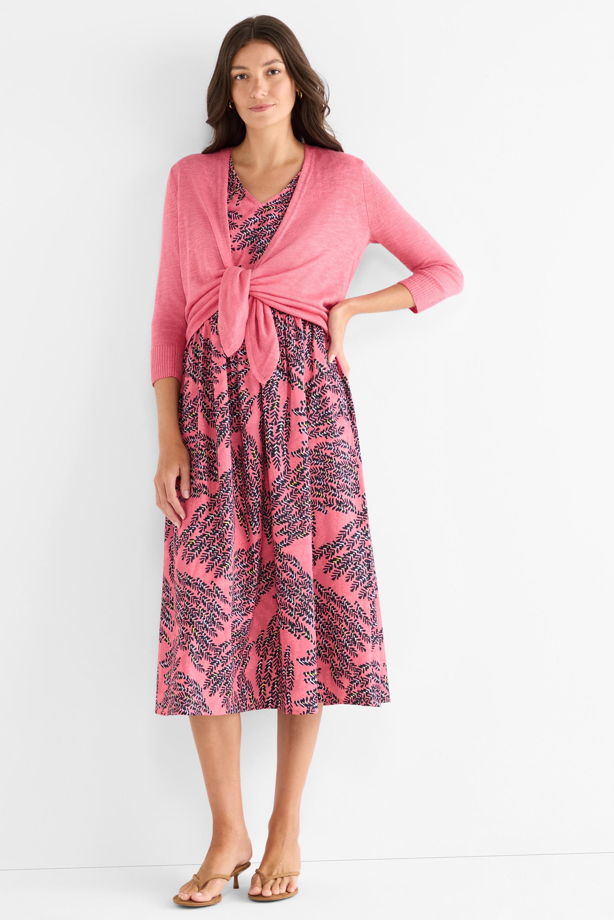 She wears a rosy leaf print midi dress and a matching pink tie-front cardigan with three-quarter sleeves.