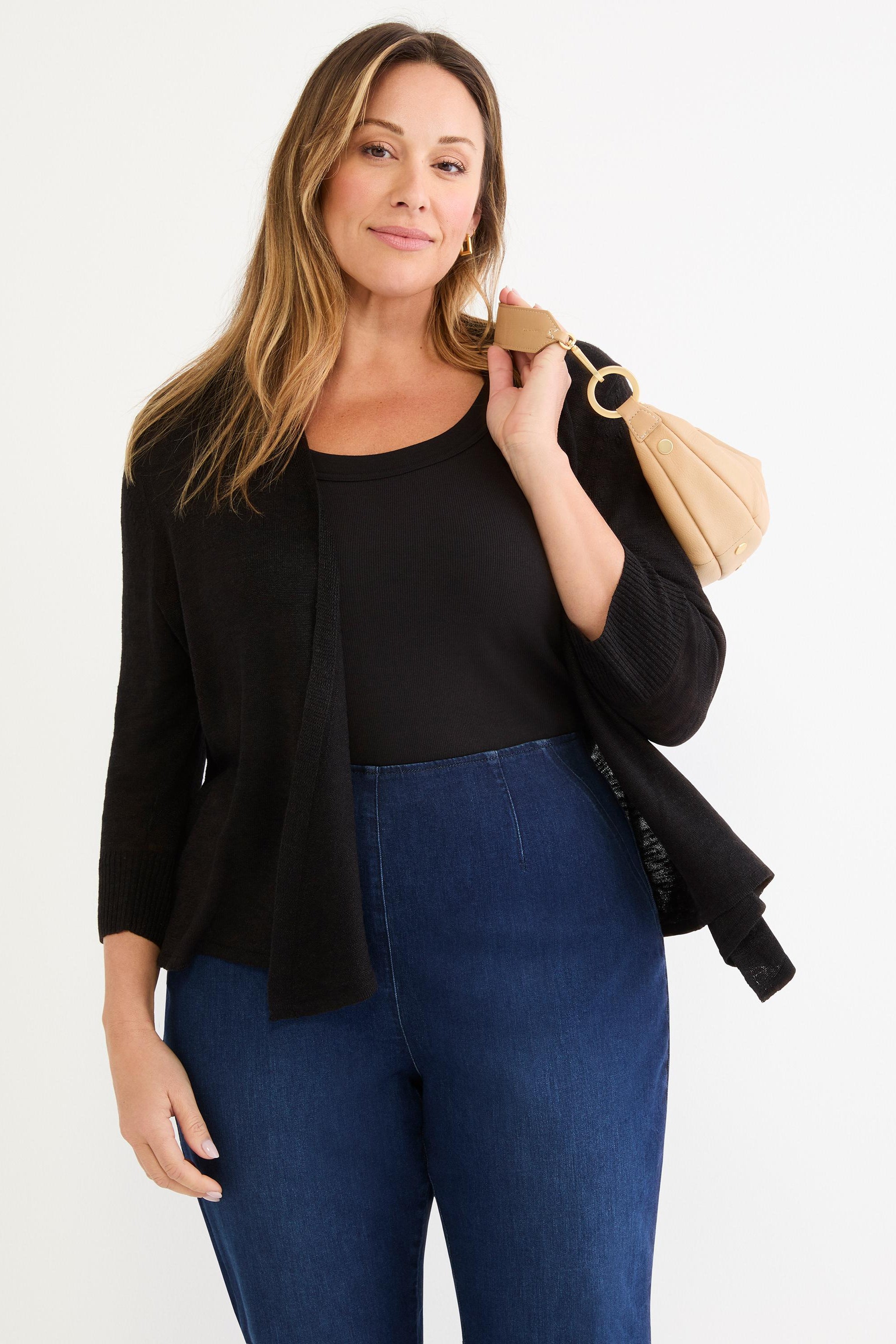 A black open-front sweater shrug with three-quarter sleeves and a draped hem is paired with high-waisted dark wash denim.