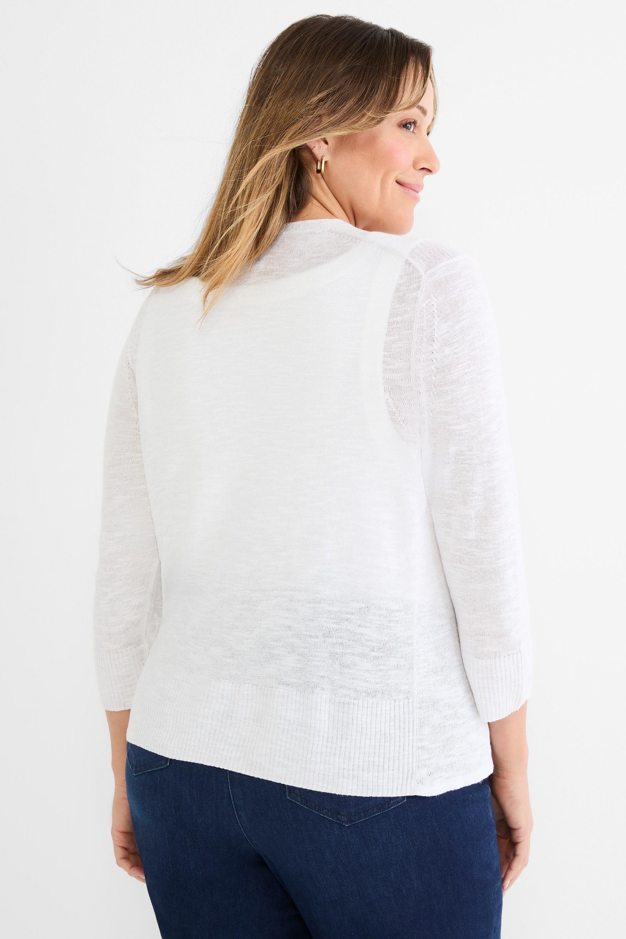 She wears a relaxed fit white knit cardigan with 3/4 length sleeves and a ribbed hem over dark jeans.