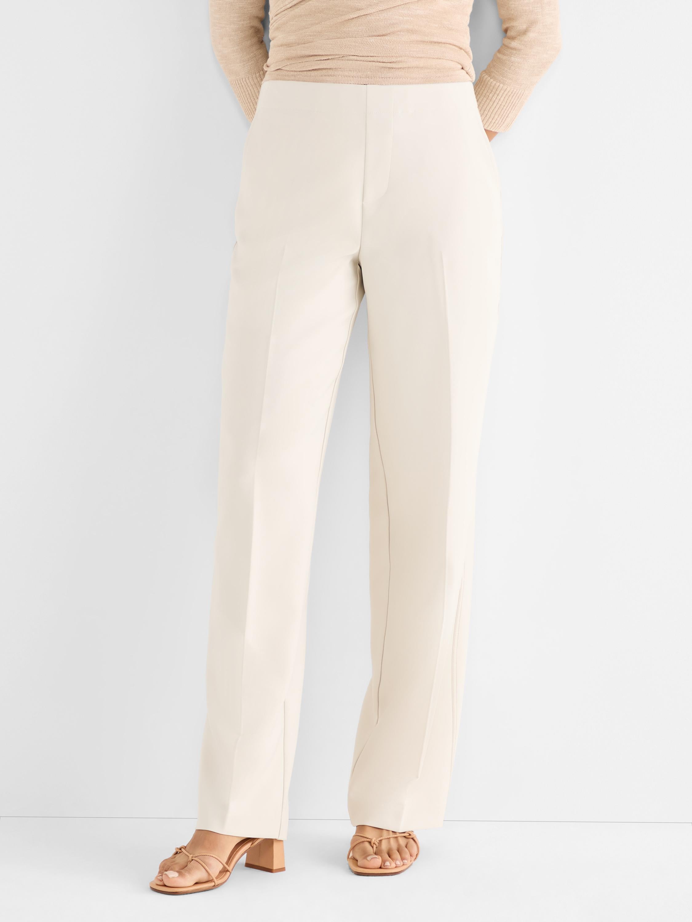 Model wears high-waisted tailored cream trousers with a straight leg and prominent front seams.