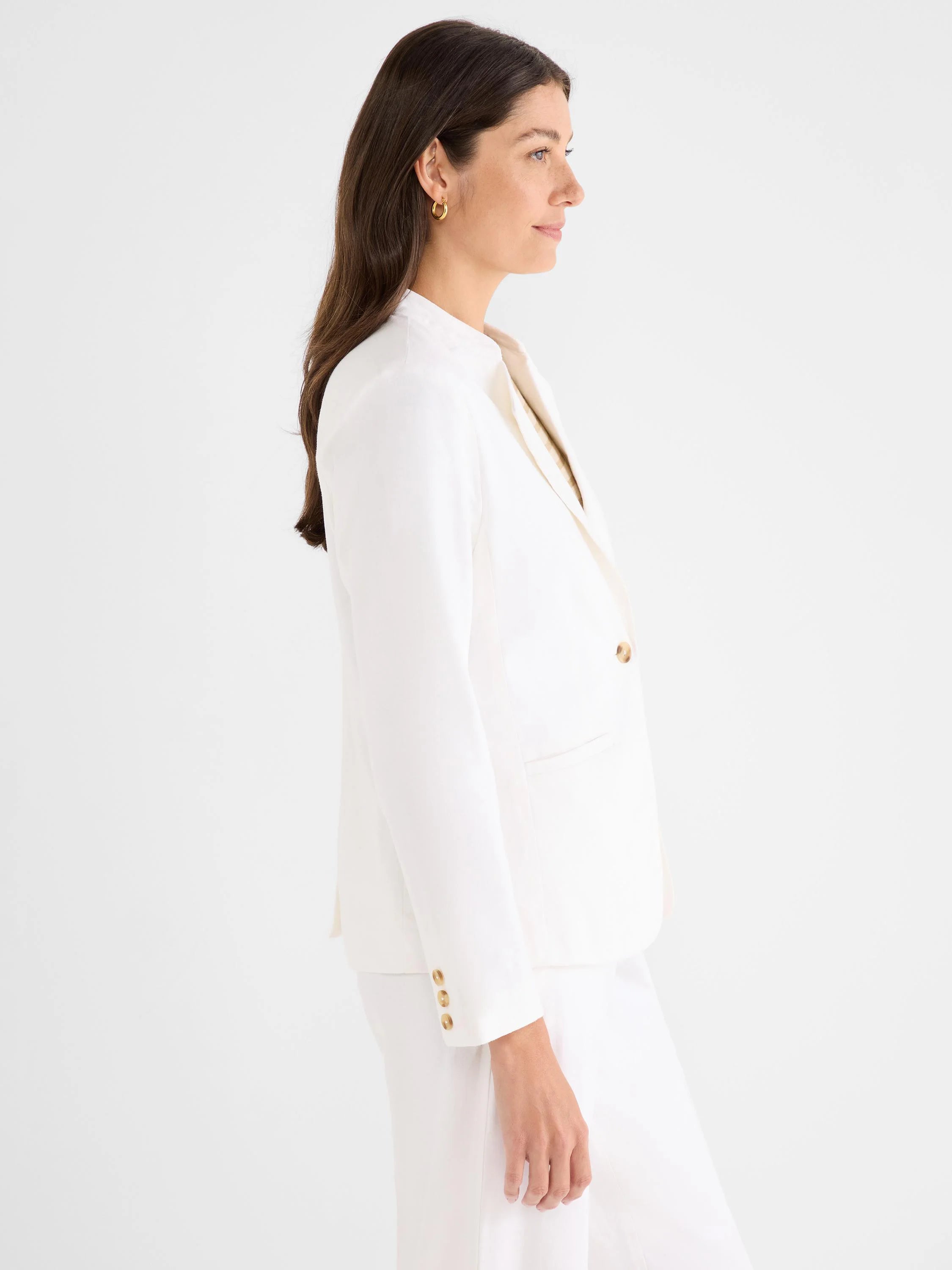 Off-white blazer with an open front, gold buttons, and flap pockets, modeled in profile.