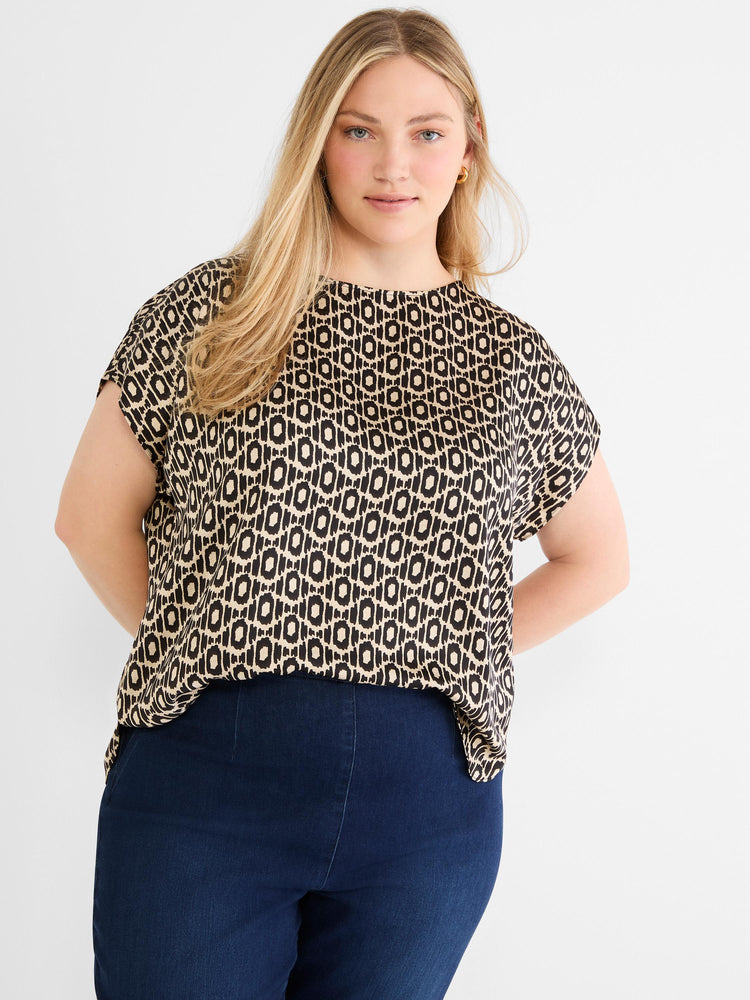 A boxy black and tan abstract print blouse with short sleeves is worn by the model with dark navy denim.