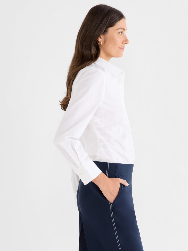 White fitted long-sleeve collared shirt is tucked into high-waisted navy tailored trousers with white contrast stitching.