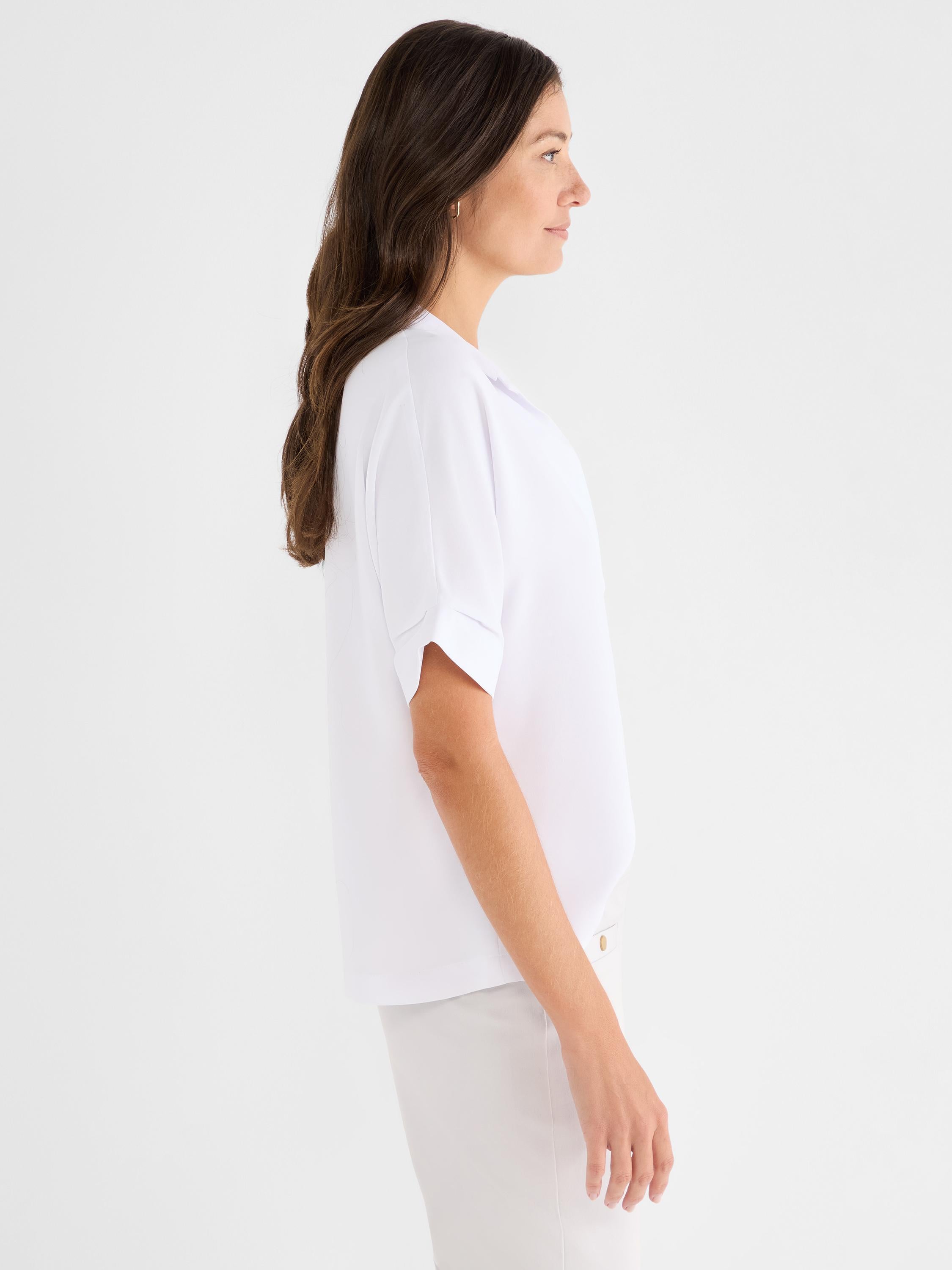 Relaxed white blouse featuring a soft notched collar and cuffed short sleeves, worn in profile.
