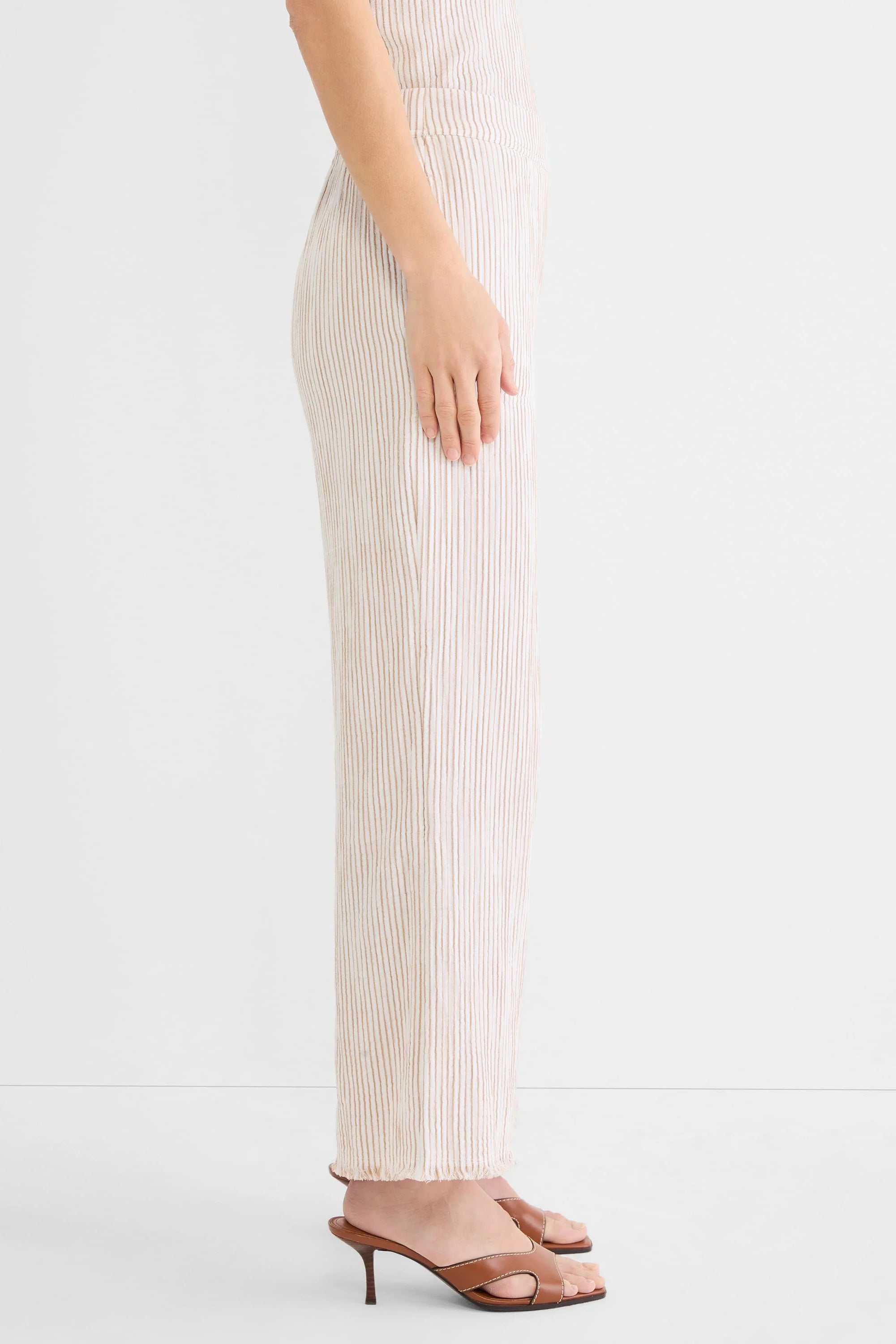 Cream wide-leg gauze pants with brown vertical pinstripes and a frayed hem. Model wearing.