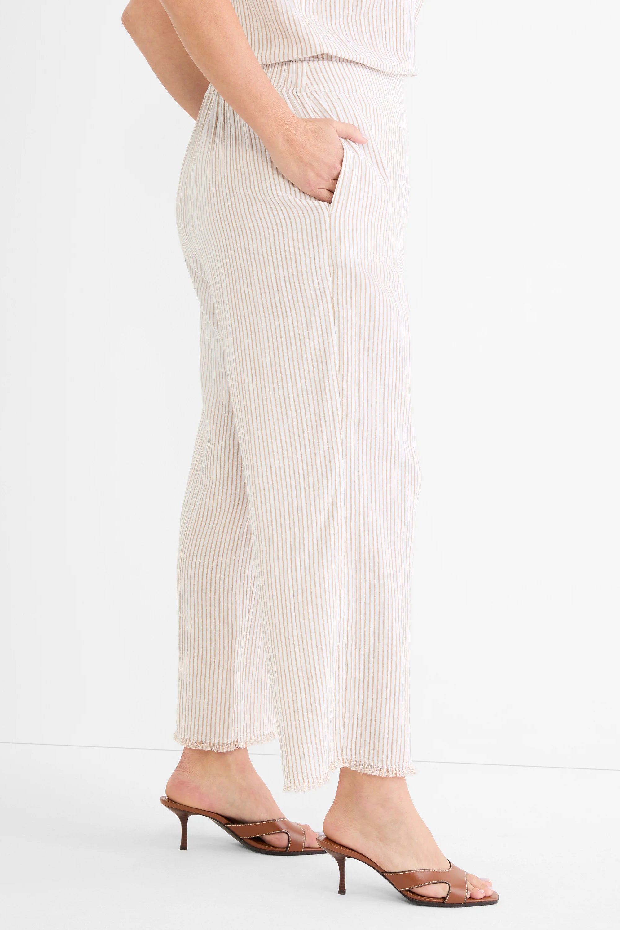 Ecru wide-leg pants with thin brown pinstripes. Features elastic waist, side pocket, and frayed hem.