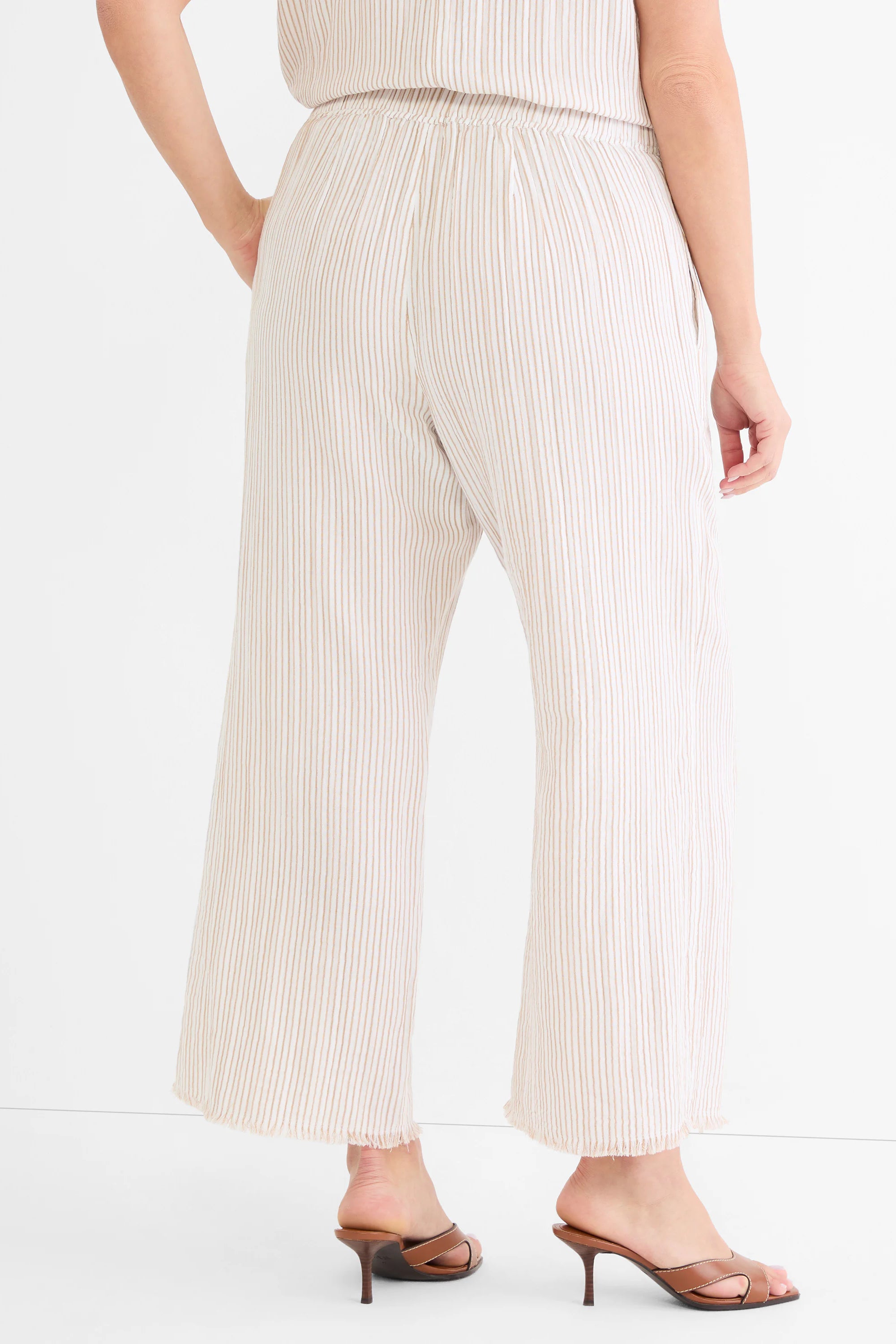 Cream wide-leg gauze pants with thin tan pinstripes, an elastic waist, and frayed hems, shown from behind.
