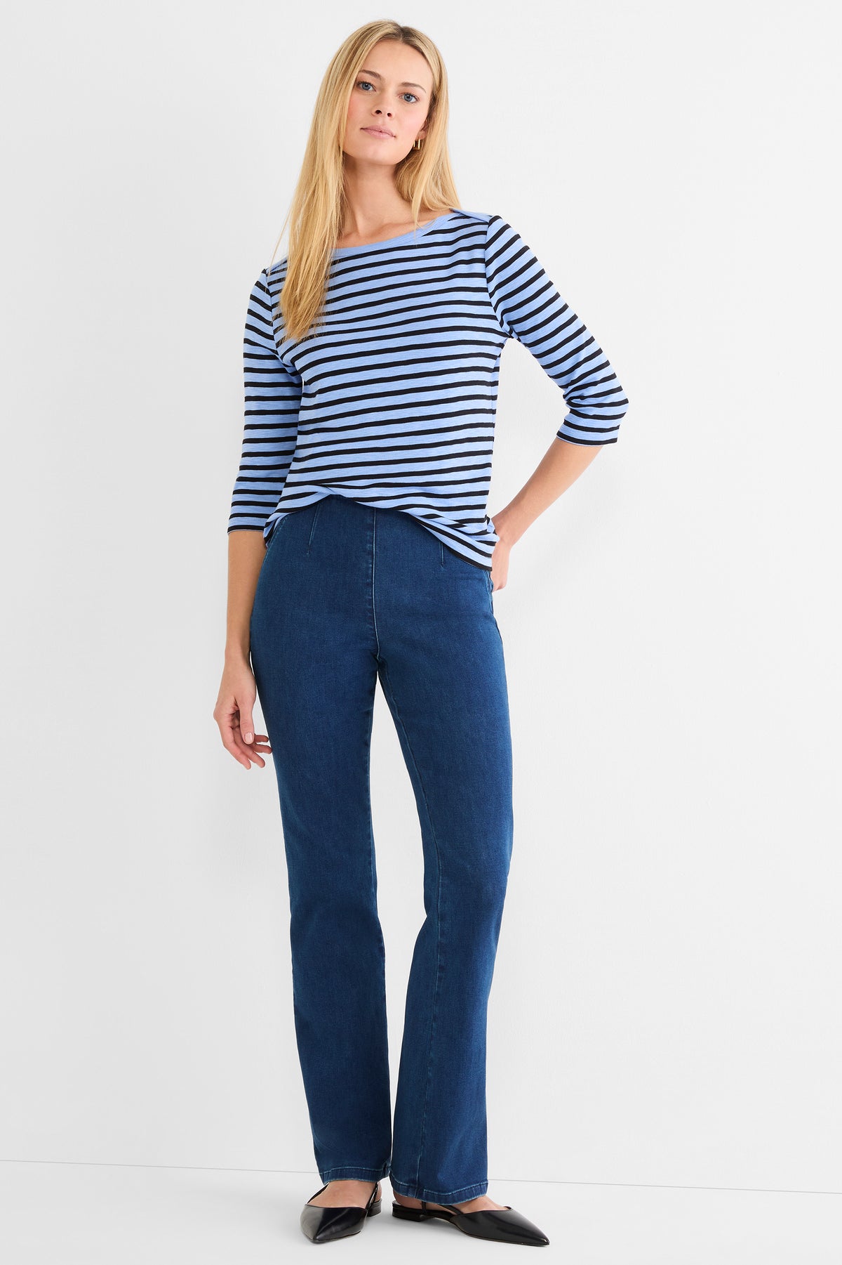 A fitted blue and black striped 3/4-sleeve top is paired with high-waisted, dark wash bootcut jeans.