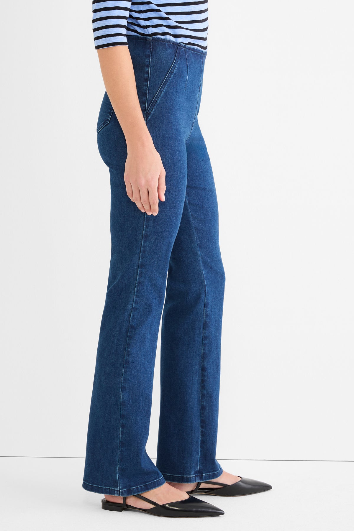 Dark wash pull-on denim jeans feature a slim fit, high waist, subtle flare, and structured diagonal front seams.