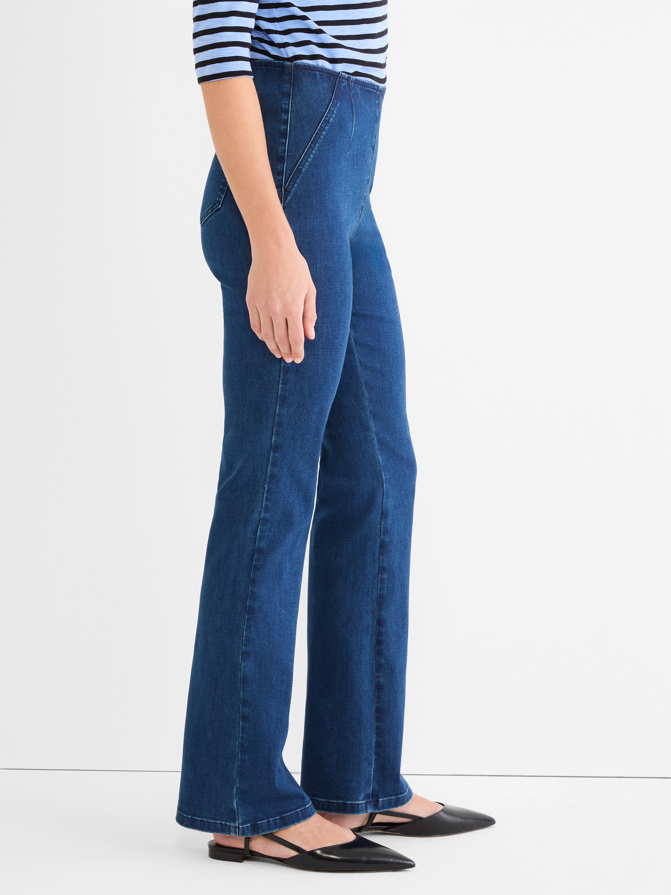 Dark wash pull-on denim jeans feature a slim fit, high waist, subtle flare, and structured diagonal front seams.