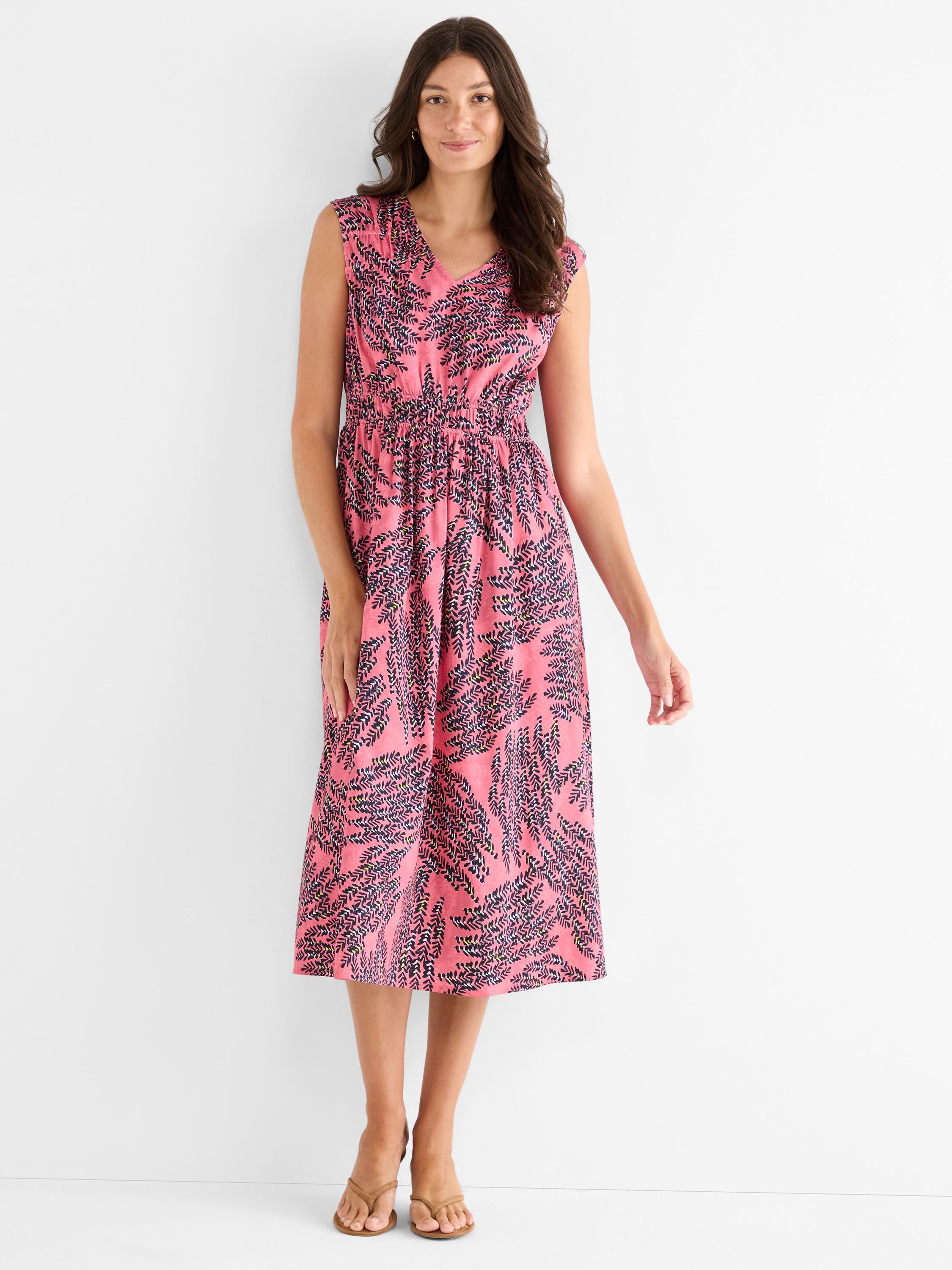 A pink sleeveless midi dress with a V-neck and a dark botanical print highlights the smocked elastic waist.