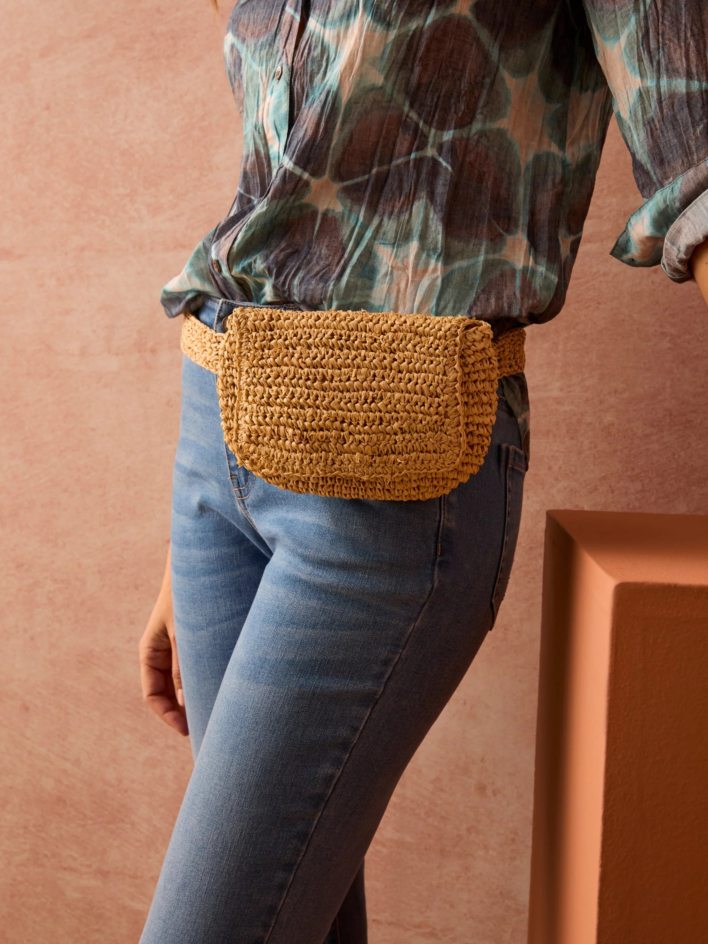 Light beige crocheted straw belt bag. Worn over blue jeans.