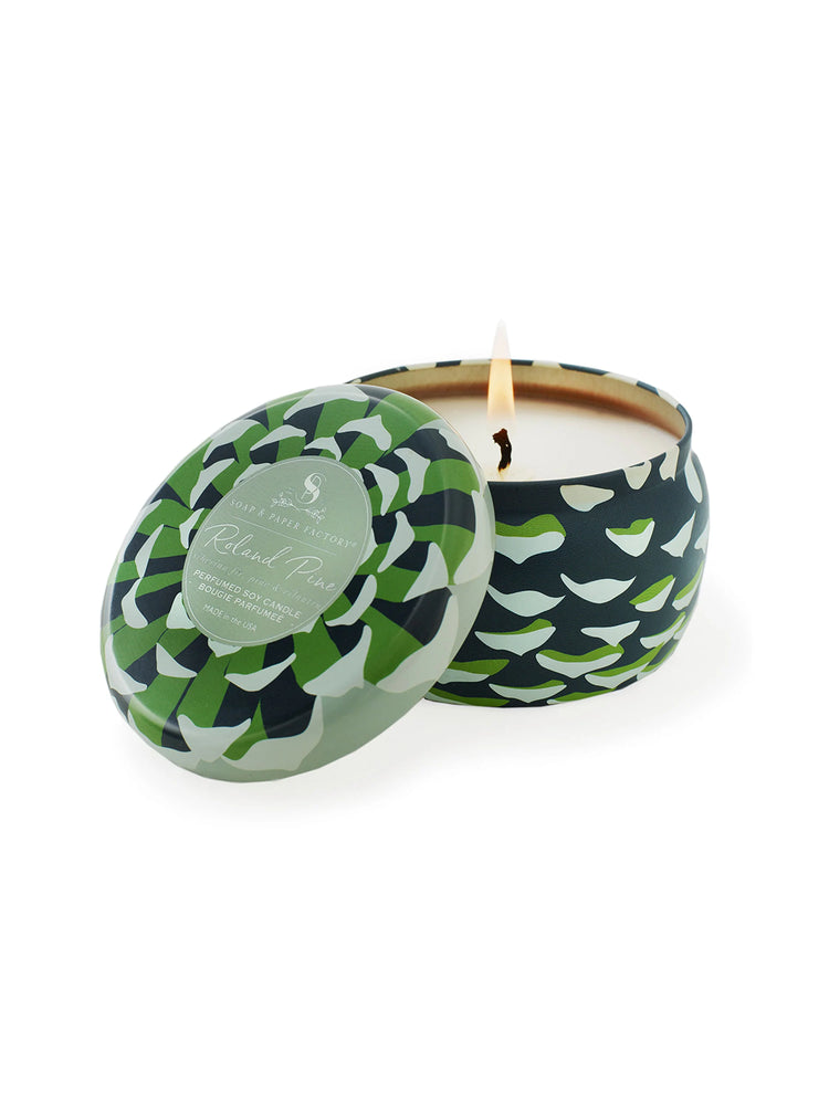 Soy candle in dark teal tin with light green & white pine cone design. Off-white candle wax; lit wick.
