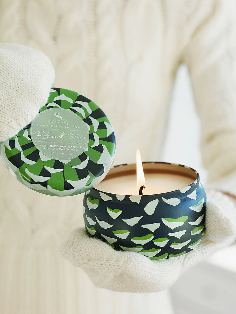 Soy candle in dark teal tin with green & white pine cone design. Lit candle shows beige wax.
