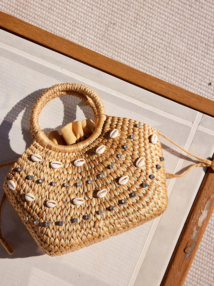 Tan woven straw bag with shell and rhinestone accents. Top handle. Light beige drawstring interior.