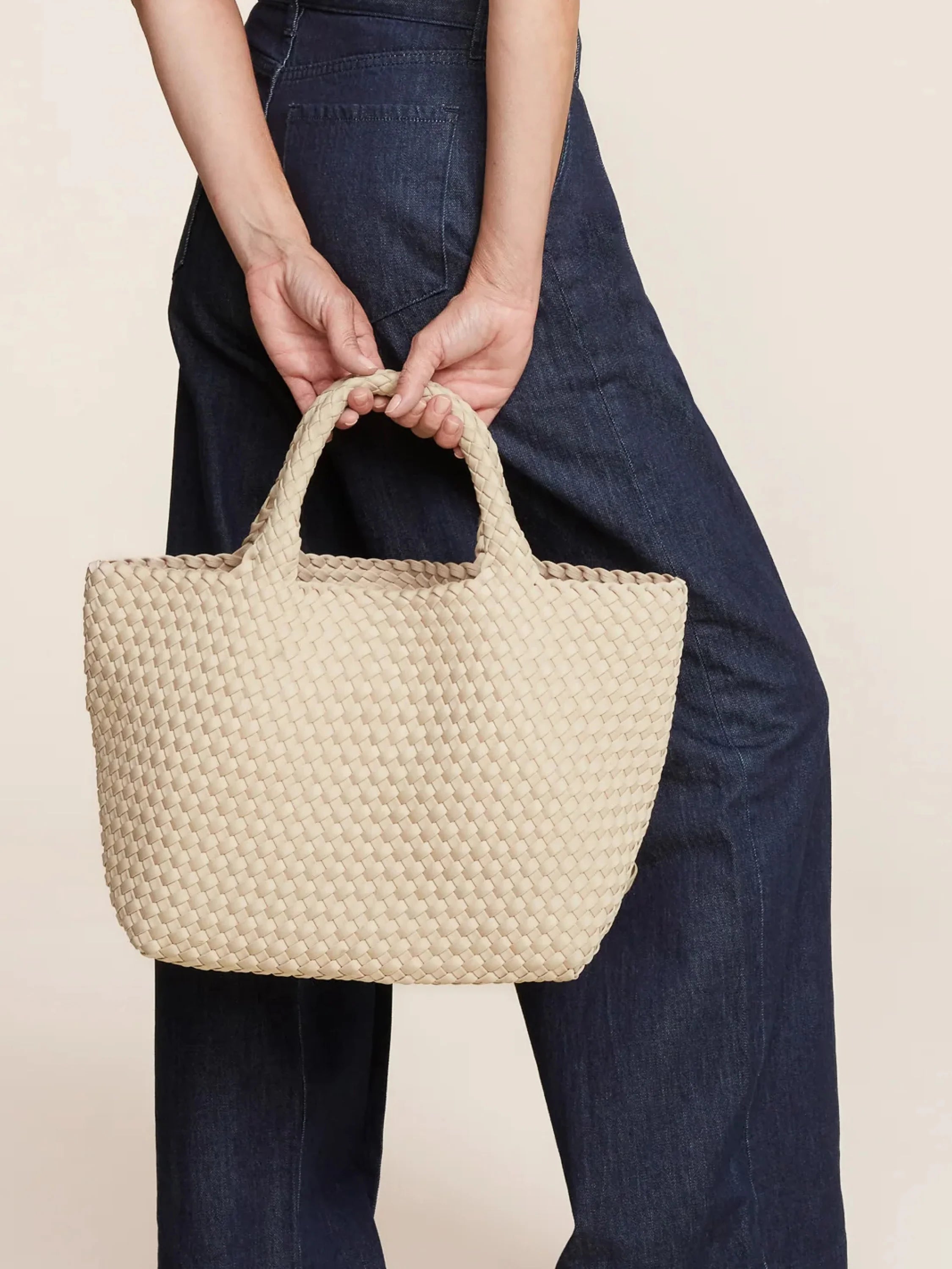 Medium cream woven tote bag with dual top handles, featuring a distinctive rectangular weave, held by a person.