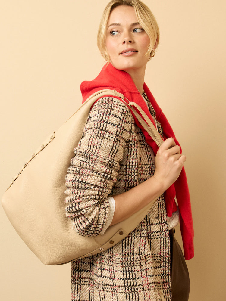 Large, pale beige pebbled leather shoulder bag with a wide strap and metallic stud accents.