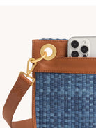 Blue woven checkerboard clutch with brown leather trim and strap, gold hardware, and phone in outer pocket.