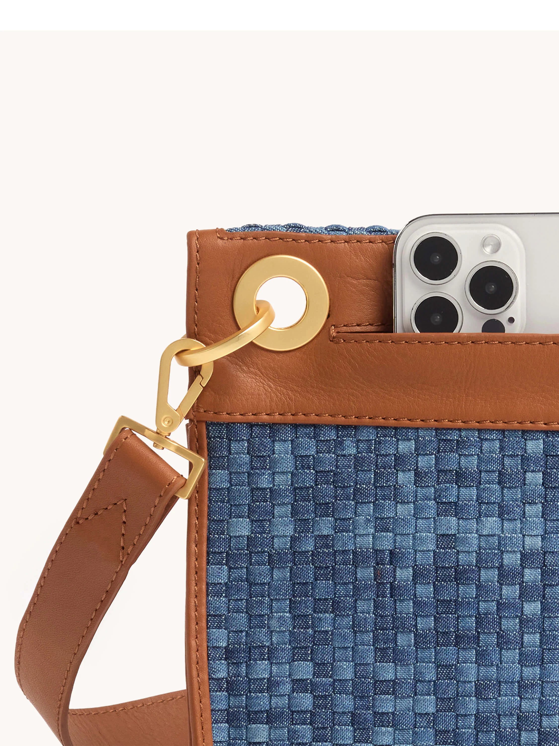 Blue woven checkerboard clutch with brown leather trim and strap, gold hardware, and phone in outer pocket.