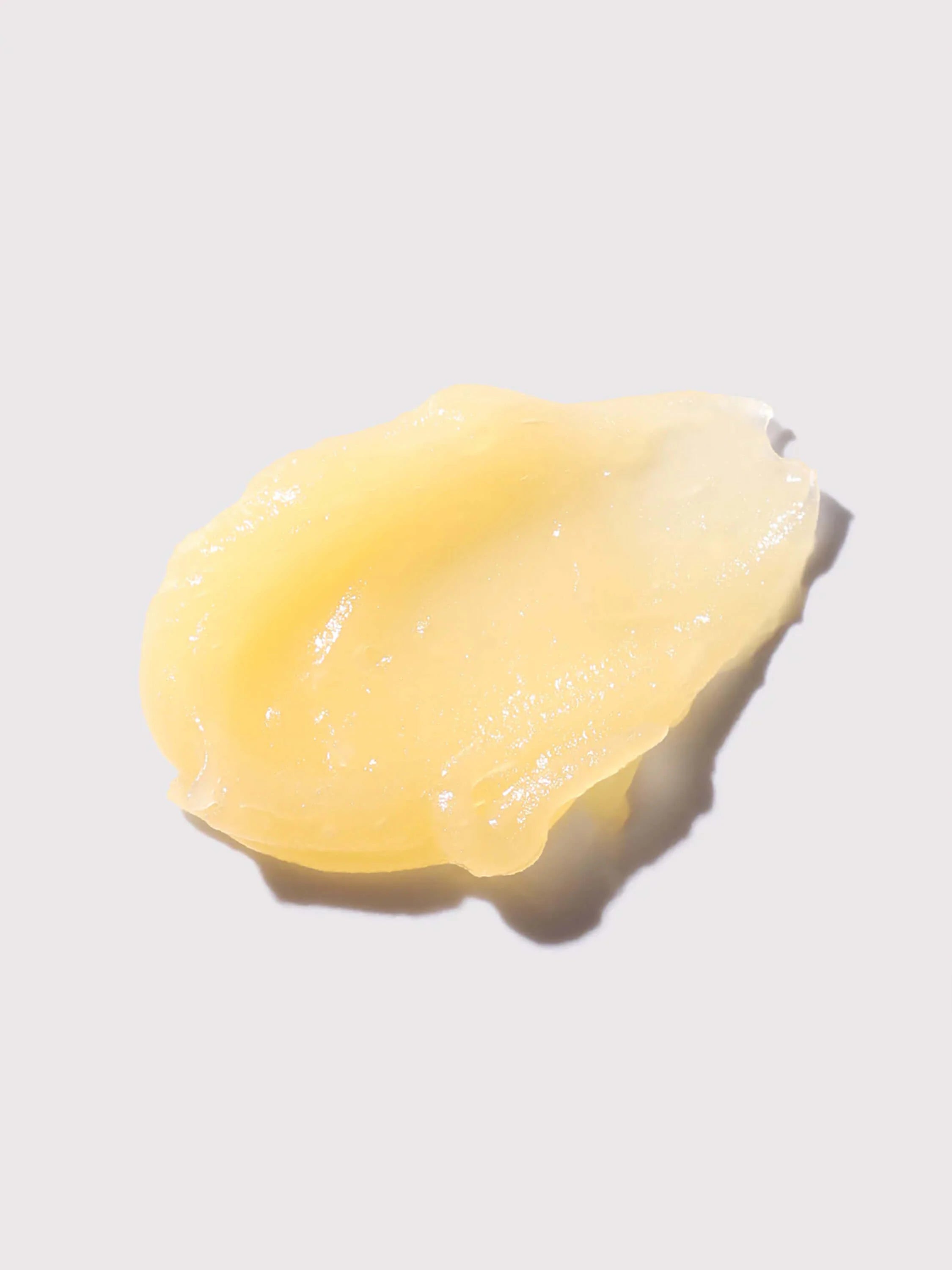 Pale yellow, glossy lip balm swatch, irregularly shaped, on a white background.