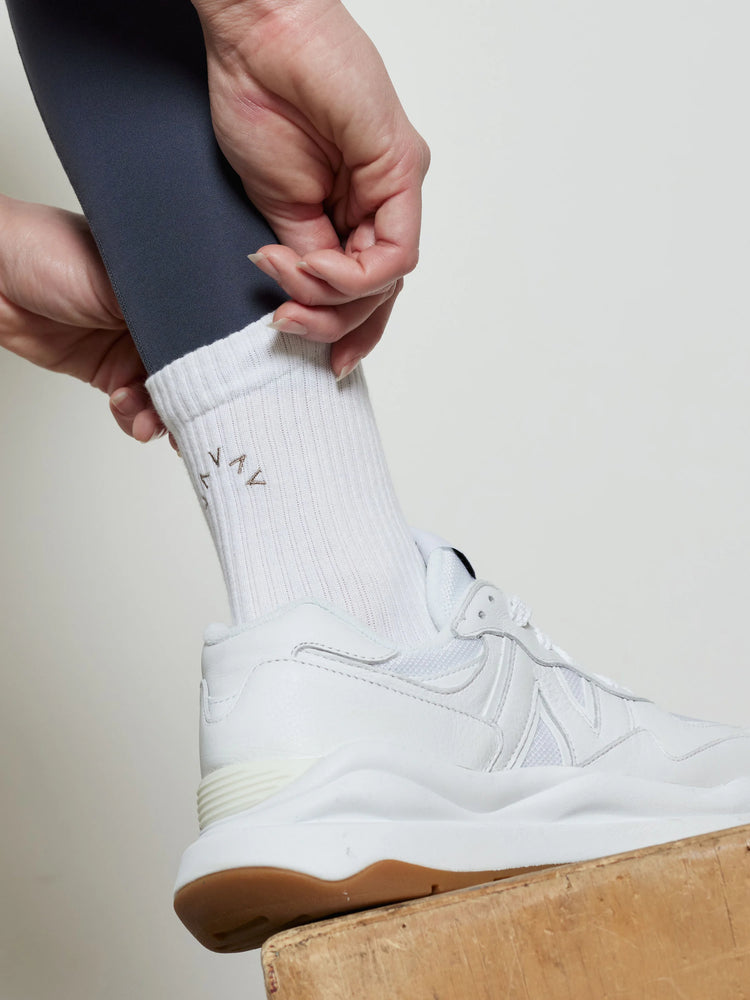 White crew socks with small, light brown logo. Shown with white shoes and dark gray leggings.