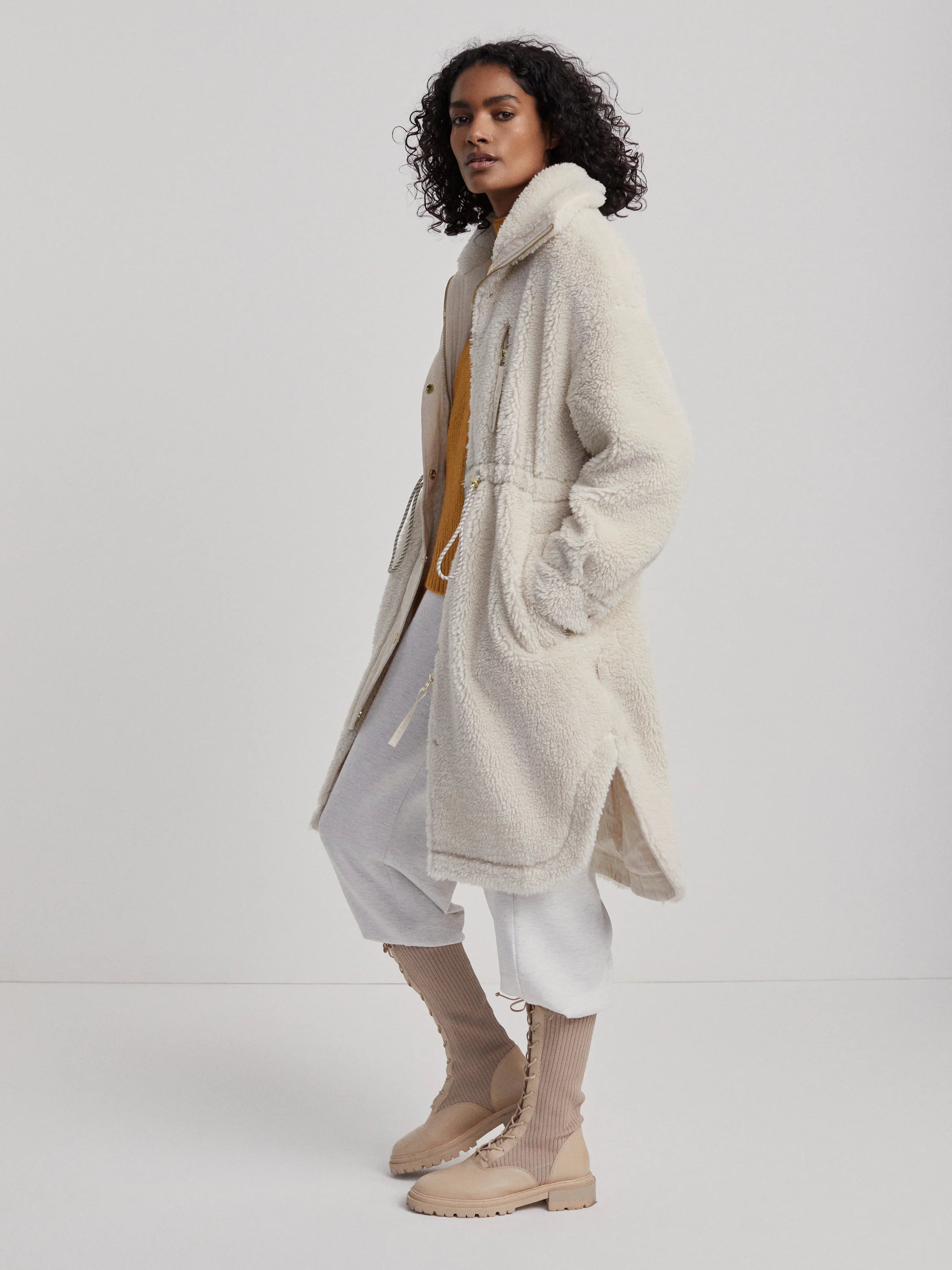 Cream midi-length sherpa coat with a high collar, full zipper, and drawstring waist.