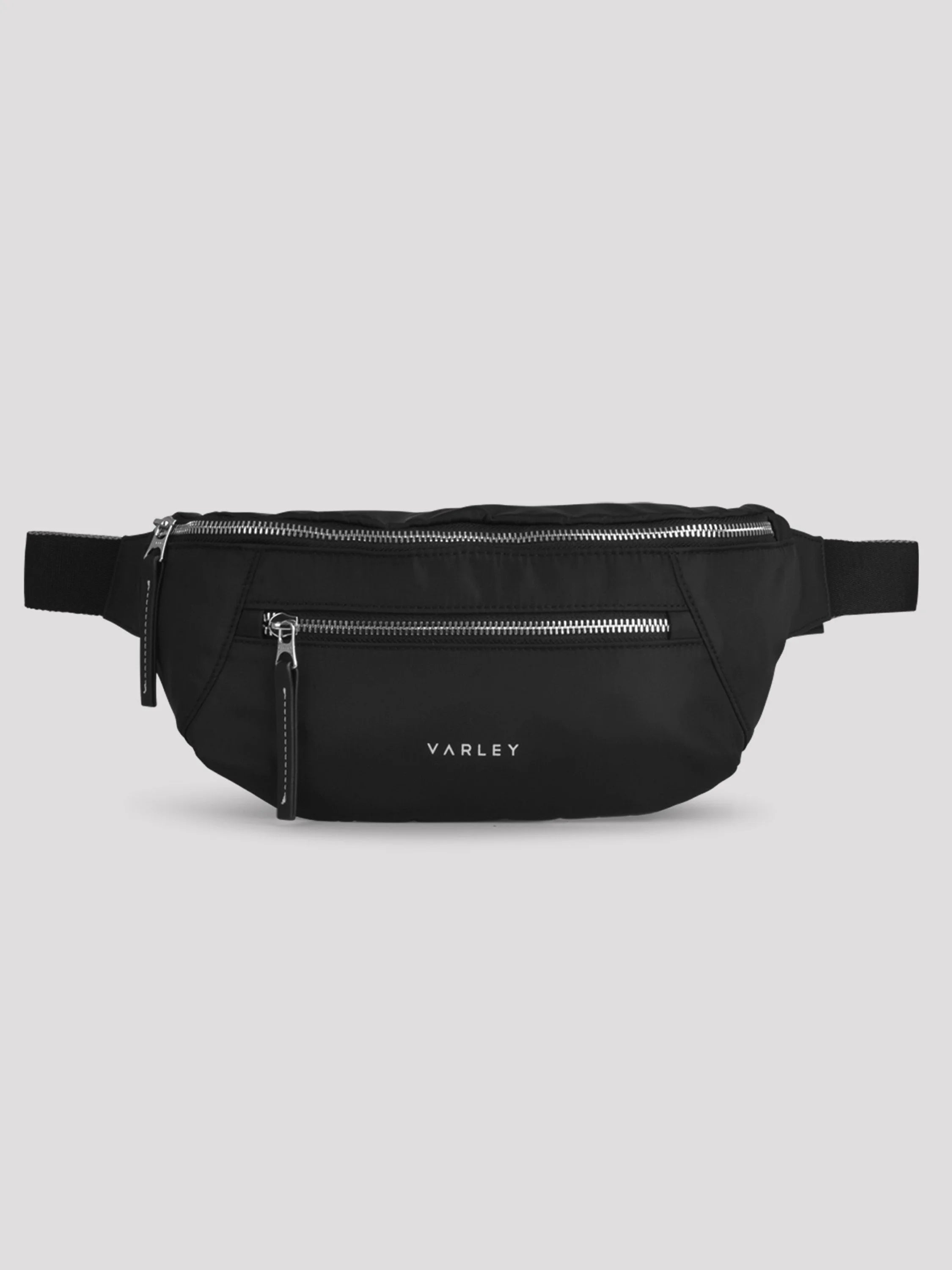Black belt bag with three silver zippers and strap. White "VARLEY" logo on front, with white accent stitching details.