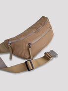 Beige curved belt bag with silver zippers and buckle.  Tan adjustable strap with black slider.