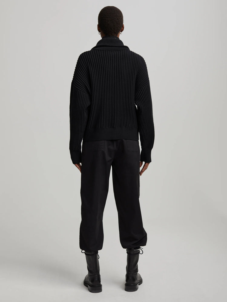 Black mock neck sweater with prominent vertical ribbing. Model viewed from the back.