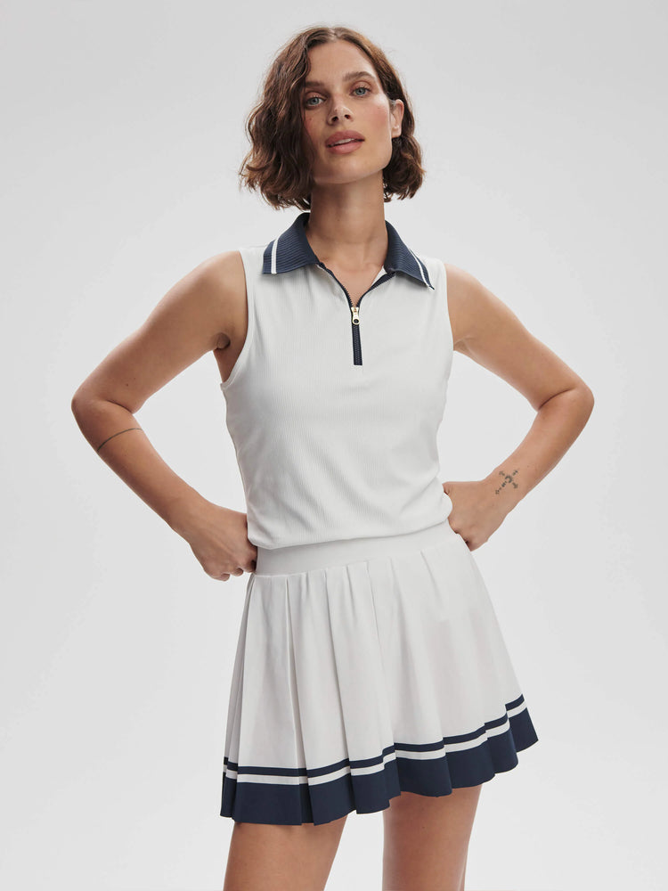 White ribbed sleeveless top with navy collar and half-zip. Matching pleated white skirt with navy trim.