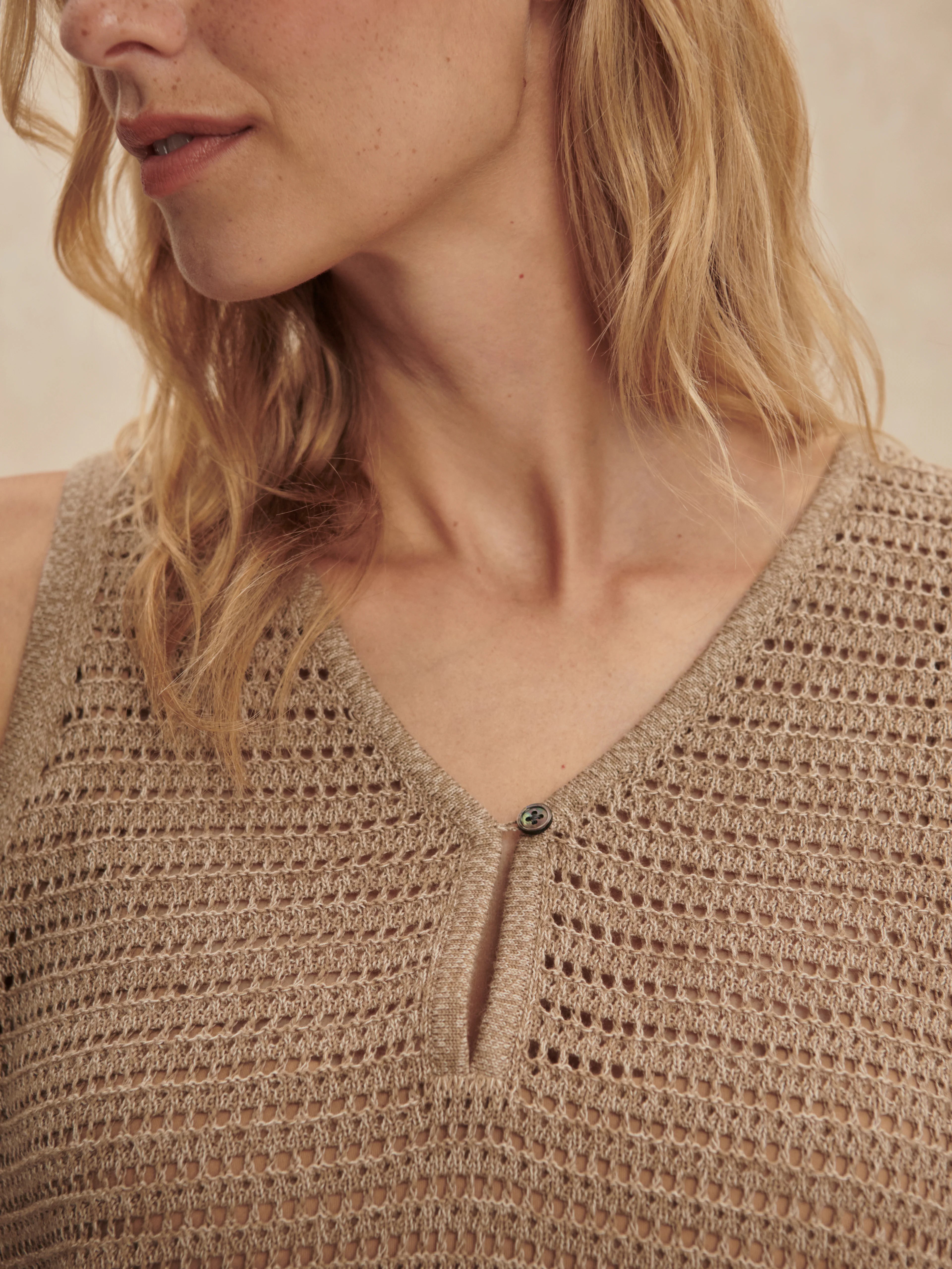Tan open-knit V-neck tank with a perforated pattern and a single dark iridescent button closure.
