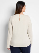 Beige long-sleeved top with subtle sparkle, keyhole back detail, and small gold button.