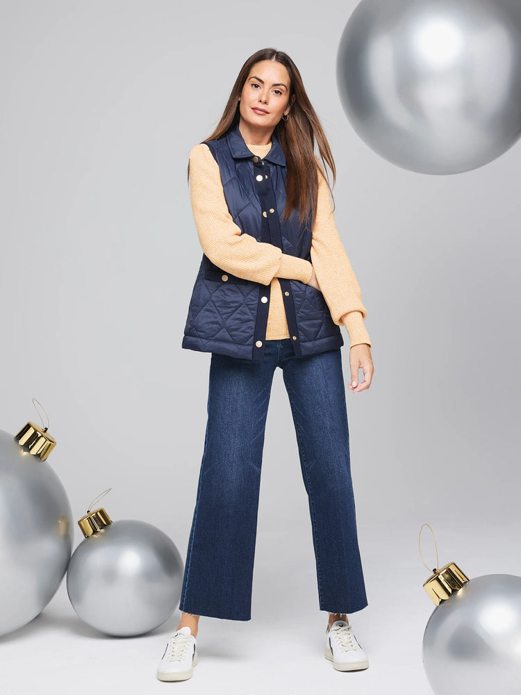 Navy blue quilted puffer vest with gold buttons. Model wears it over a pale yellow sweater.