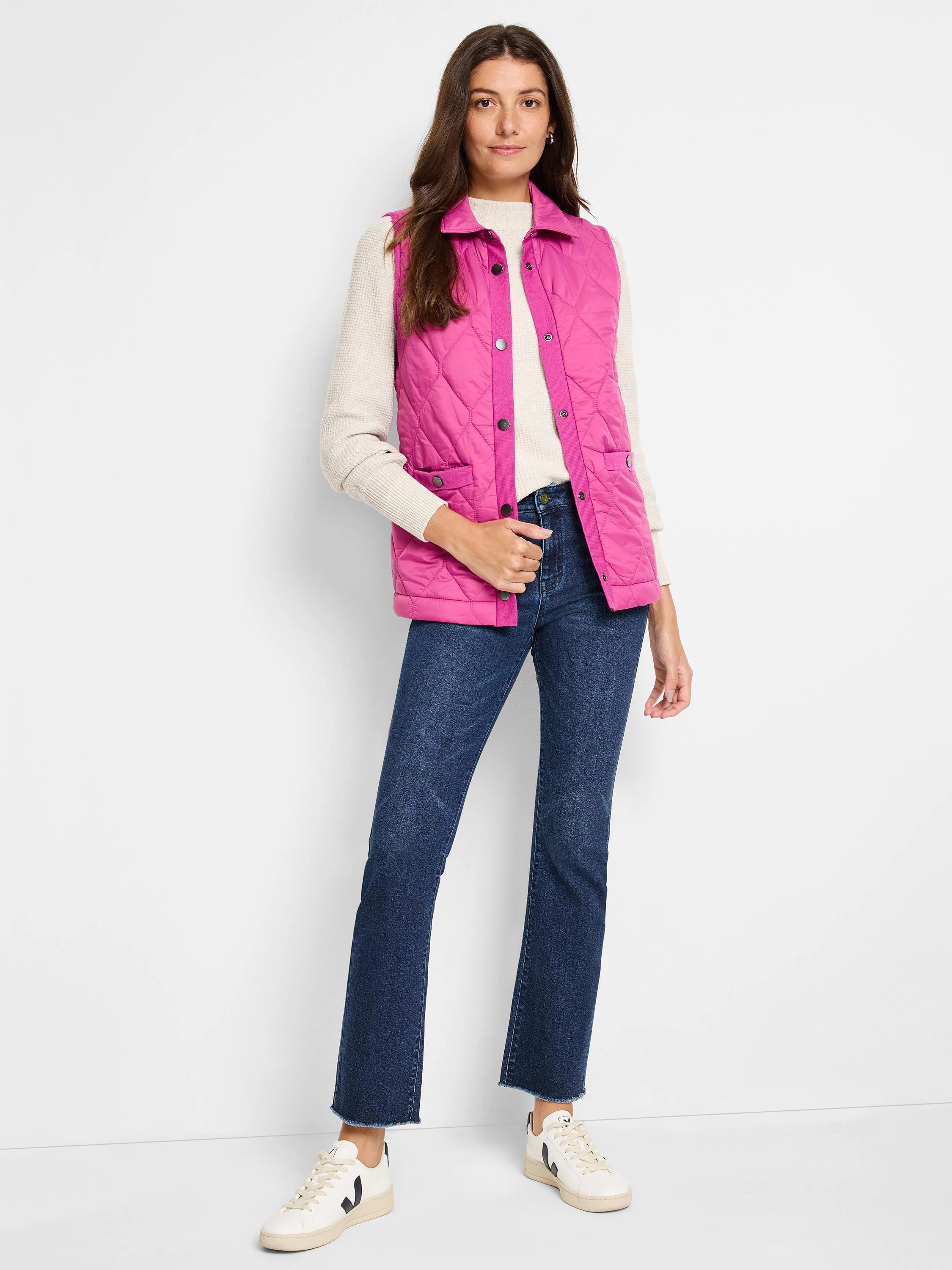 Pink quilted puffer vest with snap closures and pockets. Shown on a model with a cream sweater and dark wash jeans.