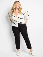 Off-white cardigan with dark-blue diagonal stripes, button front.  Model also wears black jeans and white sneakers.
