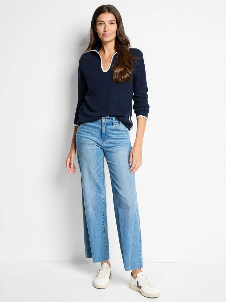 Navy blue sweater with white collar and cuffs. Model also wears light wash jeans and white sneakers.