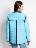 Light blue quilted puffer jacket with navy collar, cuffs, hem, and decorative navy lines on the back. Model facing away.
